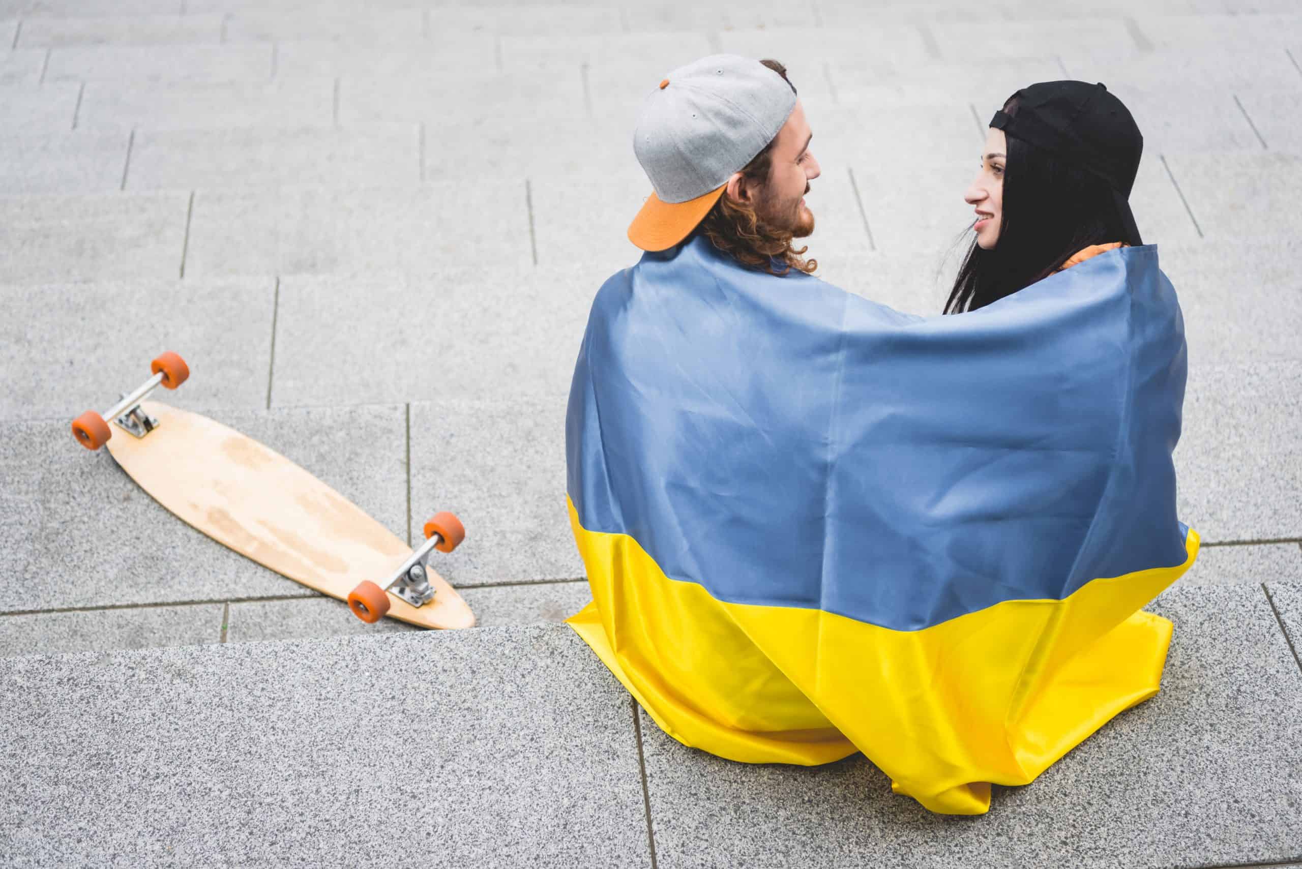 high angle view of couple with ukrainian flag sitting on stairs near skateboard, looking at each other