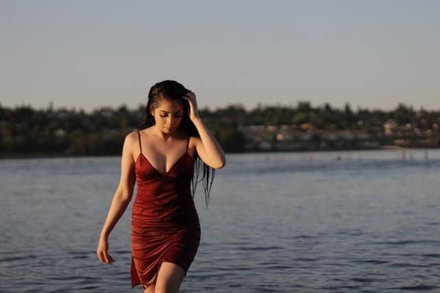 Frau mit rotbraunem Kleid spaziert im Wasser