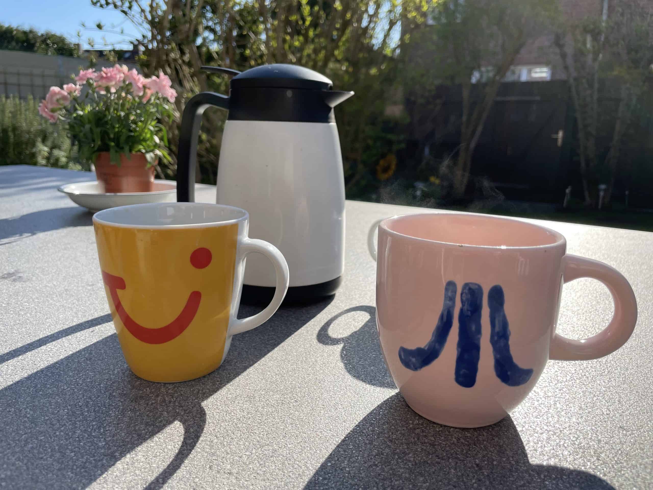 Stilleben mit 2 Bechern und Kaffeekanne auf Gartentisch