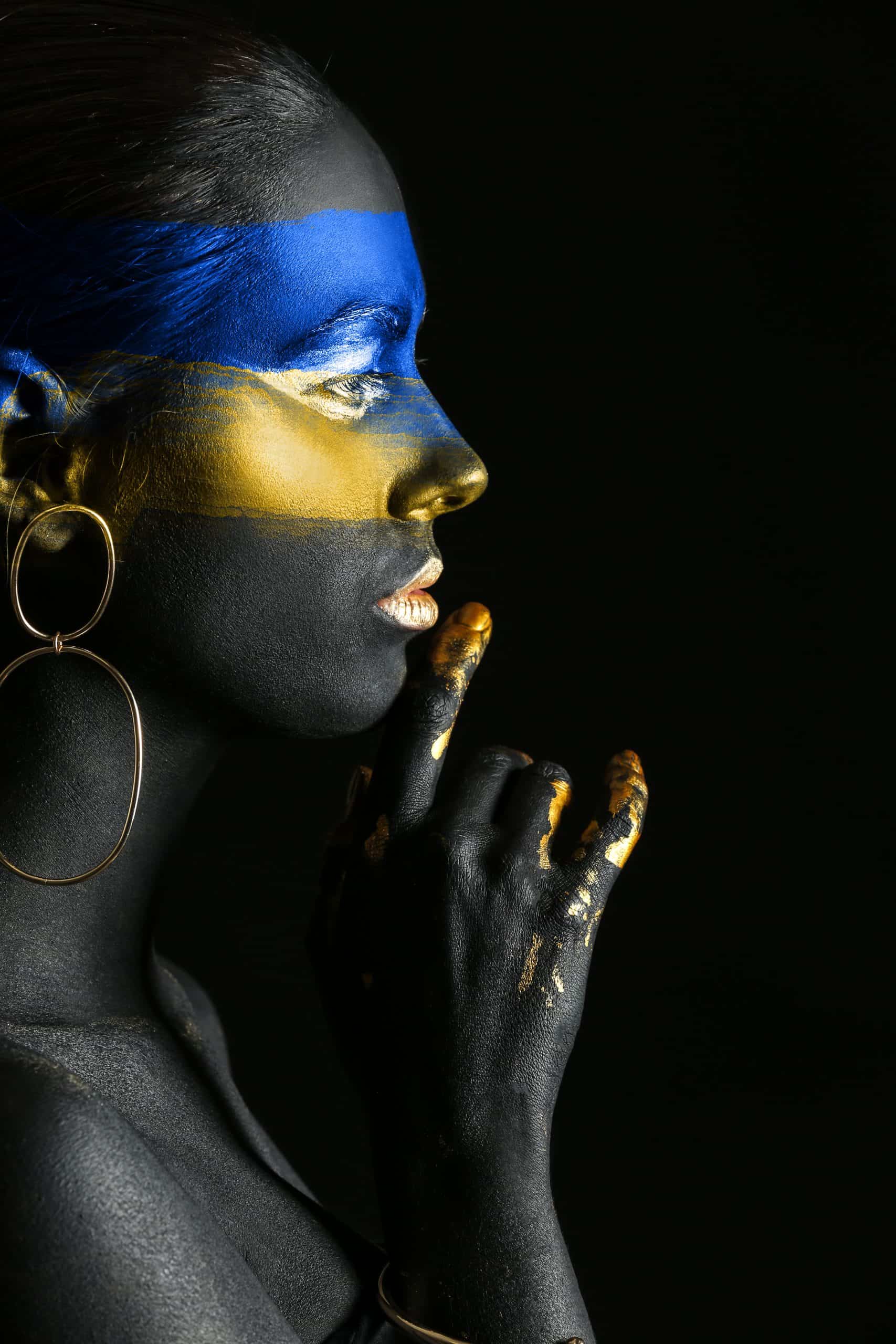 Young Ukrainian woman with blue and yellow paint on her body against dark background