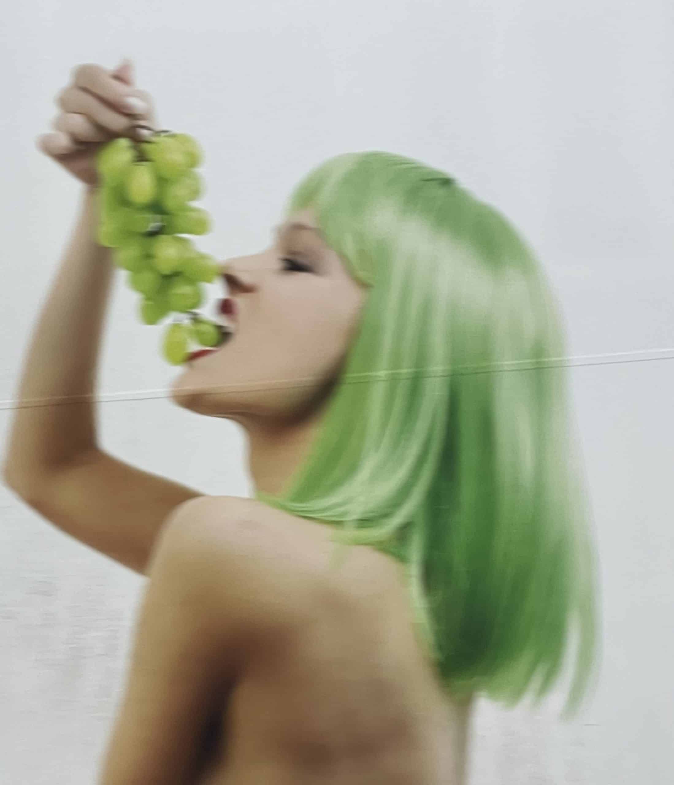 Frau mit grünen Haaren ißt grüne Weintrauben