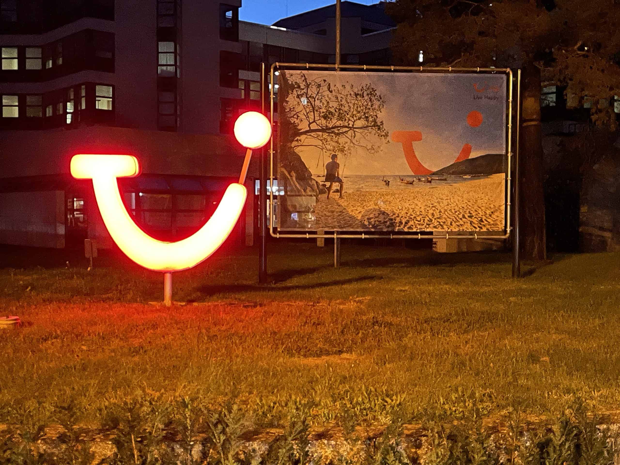 Abedlicher Blick in der Dunkelheit auf die Karl-Wiechert-Allee 23 mit helllrot leuchtendem TUI-Logo vor TUI-Werbewand. Im Hintergrund die TUI-Zentrale.