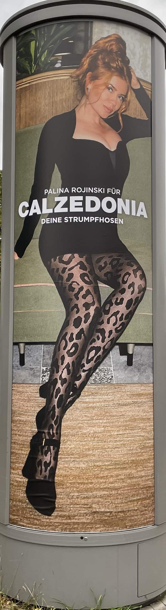 Auf der Litfaßsäule: Sexy Palina Rojinski in schwarzem, kurzem Kleid und böickdichter grauer Strumpfhiose mit schwarzem Raubkatzenmuster sowie schwarzen High Heels macht Calzedonia-Reklame.