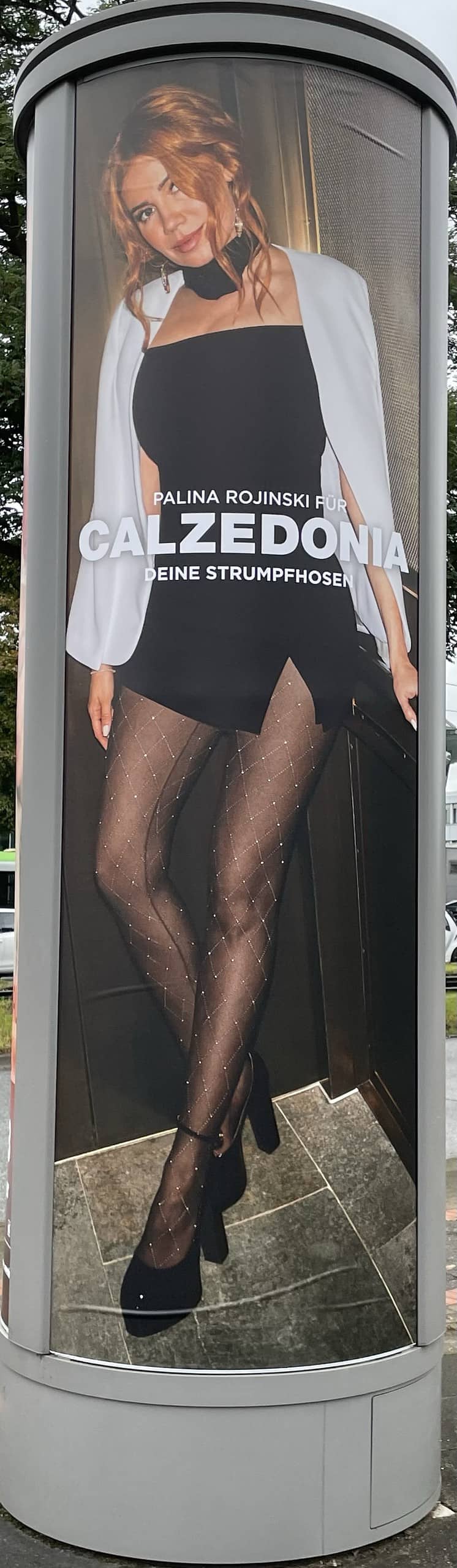 Auf der Litfaßsäule: Sexy Paline Rojinski in schwarzem, kurzem Kleid, weißem Blazer und schwarzer Perlonstrumofhose mit schwarzen High Heels macht Calzedonia-Reklame.