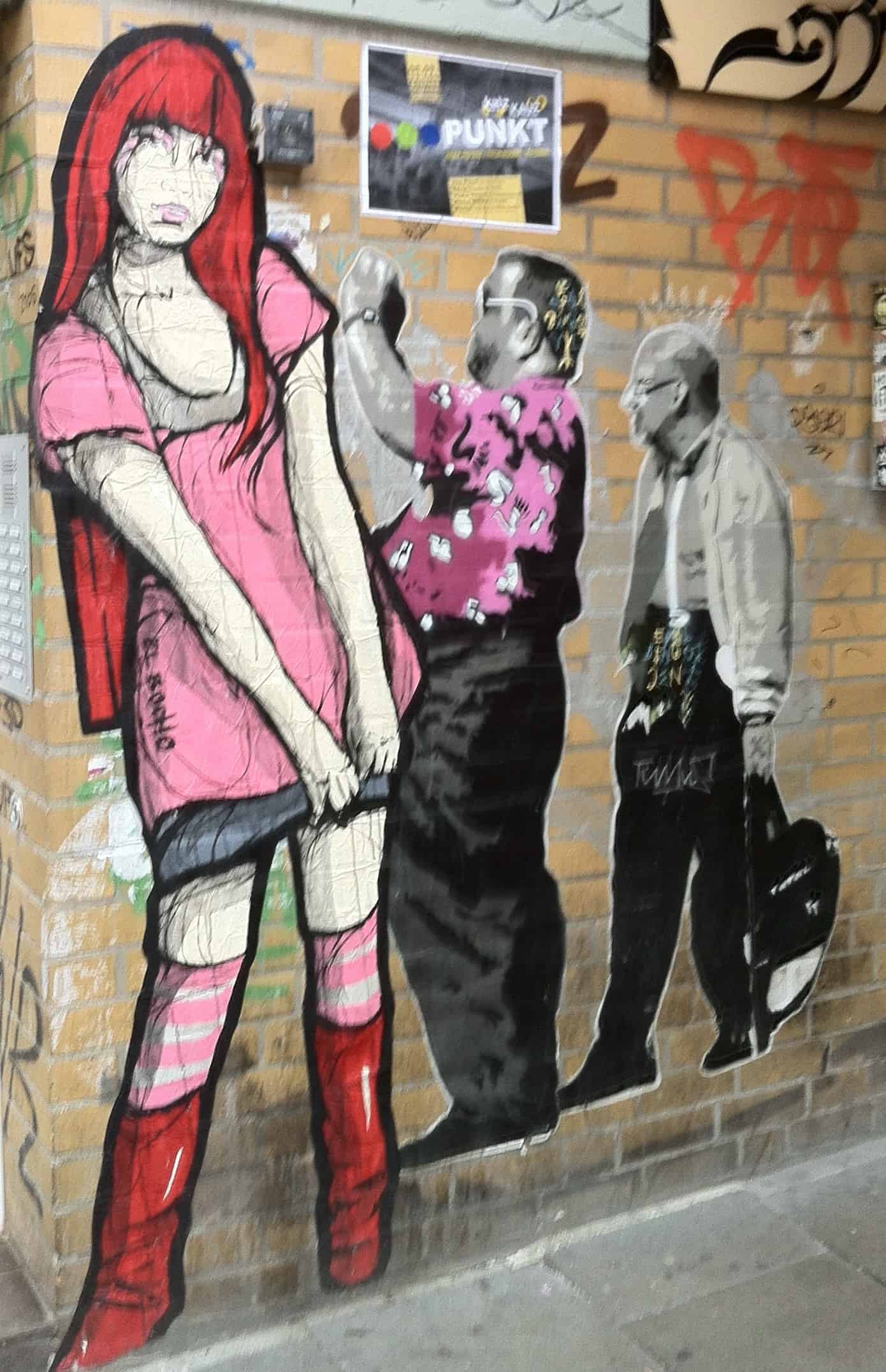 Street Art Wandkunst in der Schanze: Asiatisch anmutendes rothaariges Mädchen mit Rock, roten Stiefeln und rosa T-Shirt, daneben sie fotografierender Tourist gefolgt von weiteren schauendem Mann mit Tasche.