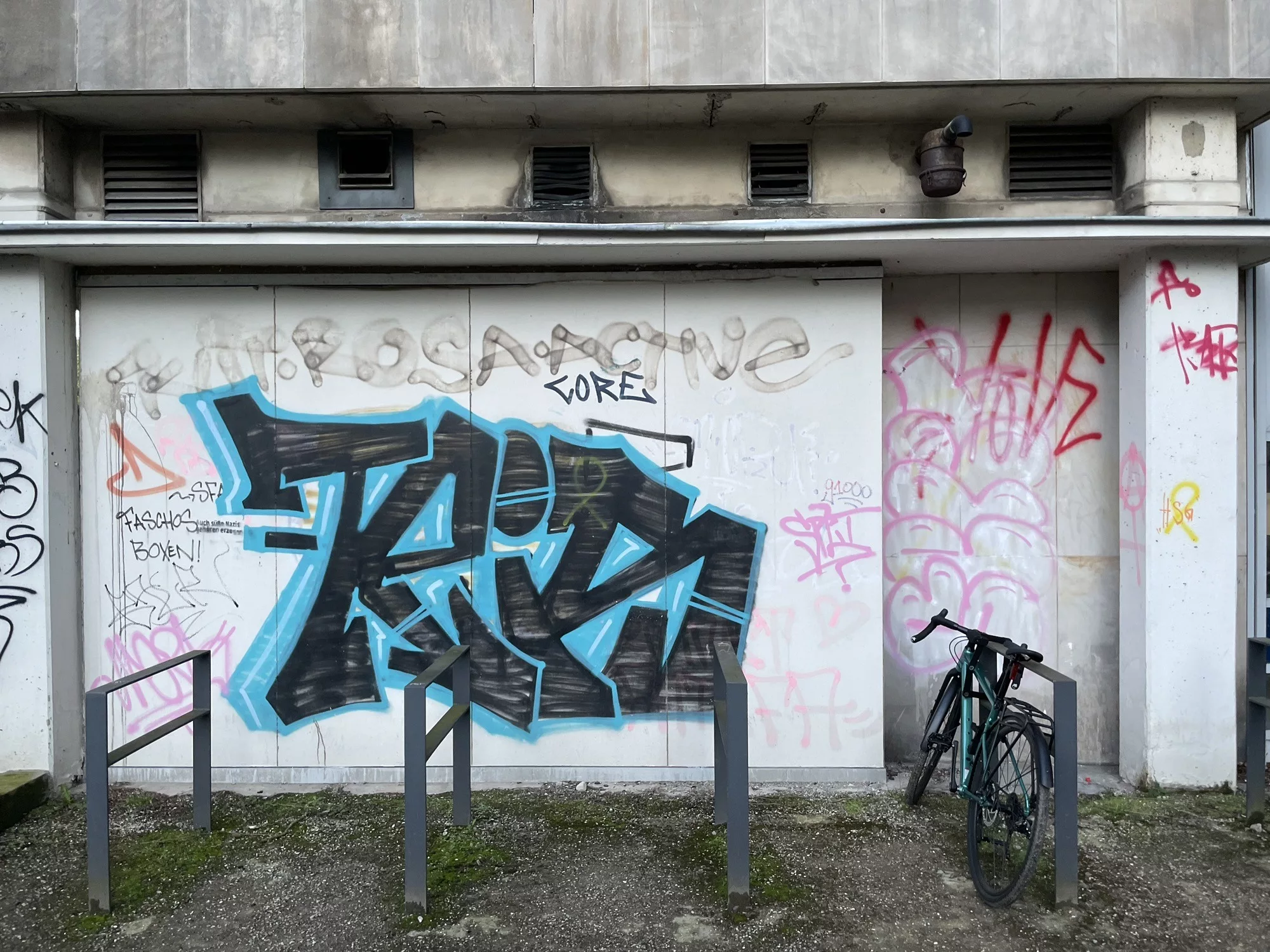 Leibniz Uni Hannover: Fahrradständer mit einem abgestelltrn Fahrrad vor heller Gebäudewand mit großem schwarz-blauen Tag umgeben von vielen kleinen Tags 