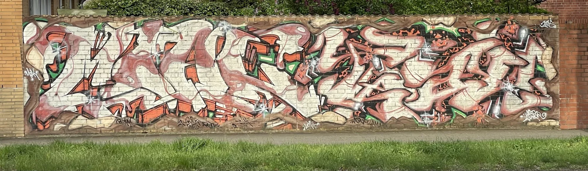 Breite aus roten Ziegeln gemauerte Mauer mit weißem Graffitischriftzug über die gesamte Mauer entlang.