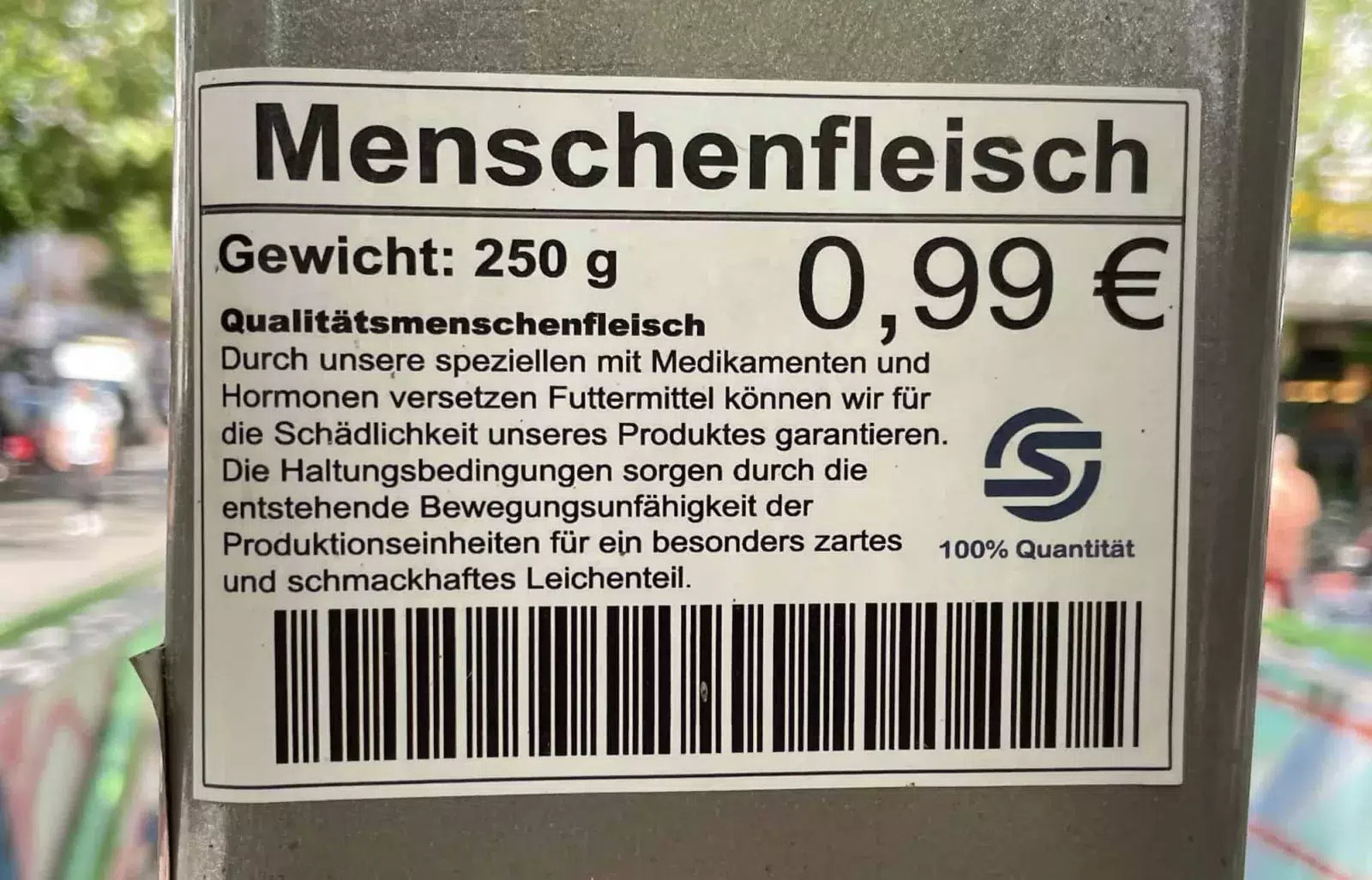 Ein satirischer Werbeaufklebr für schmackhaftes Menschenfleisch zu 0,99 EUR/250 g an einer Straßenlaterne.