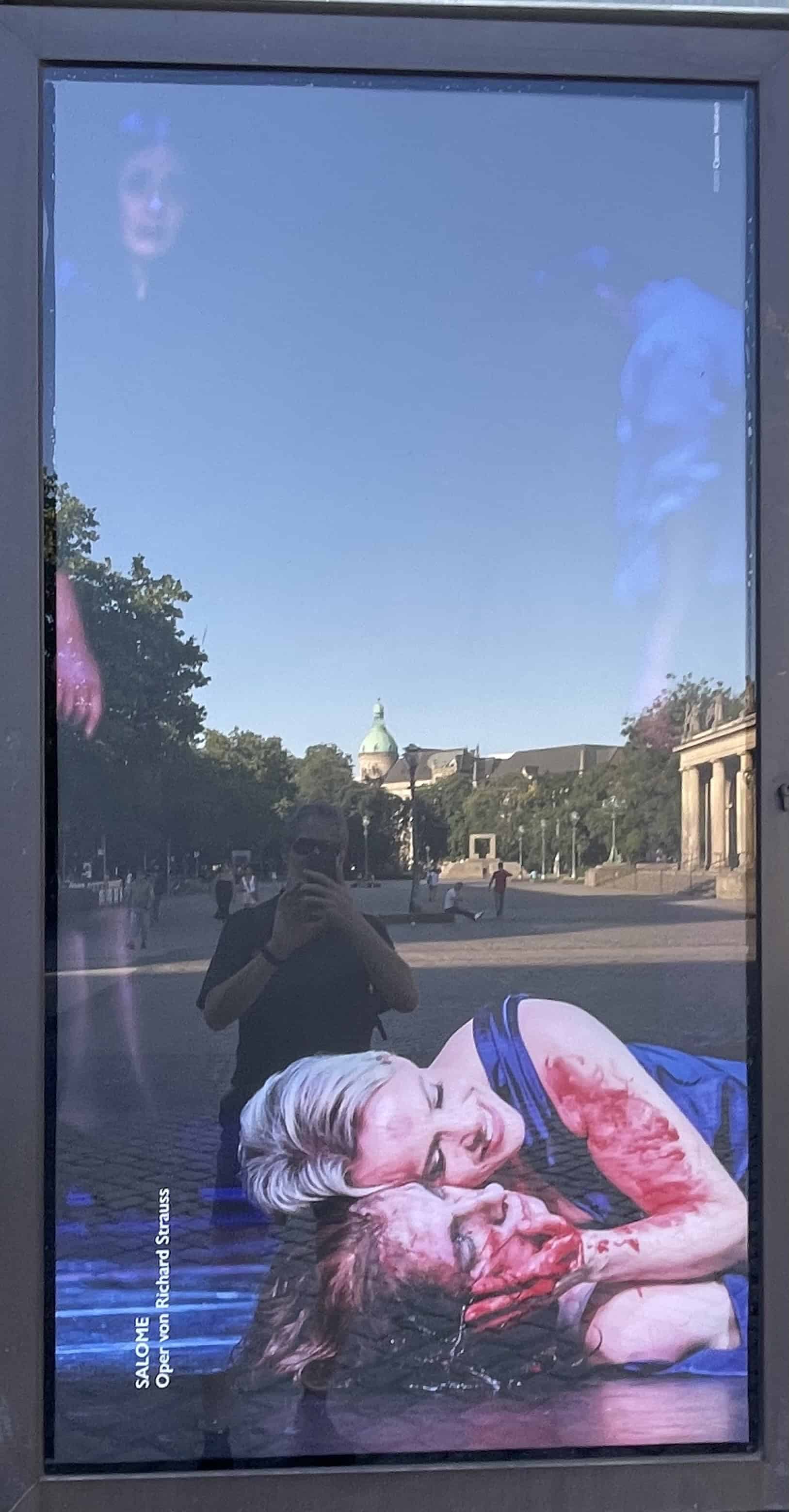 Plakat der Oper Hannover zur Oper Salome mit liegender Salome inklusive blutigem Arm und hält blutigen Kopf einer Person unter sich.