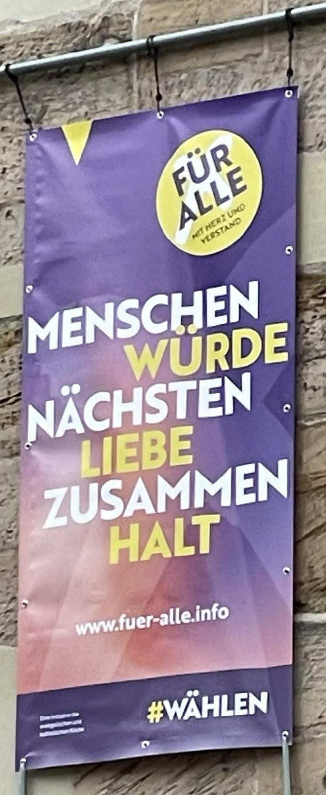 Wir Für alle Plakat an der Kirchenwand: MENSCHEN WURDE NÄCHSTEN LIEBE ZUSAMMEN HALT