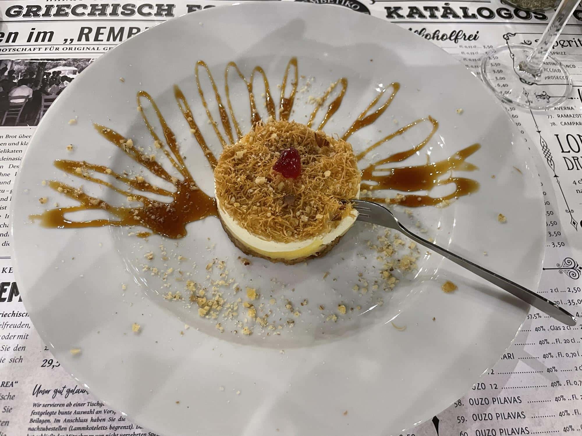 Teller griechischer Nachspeise Ekmek auf Tischdecke mit Zeitungsdruck.