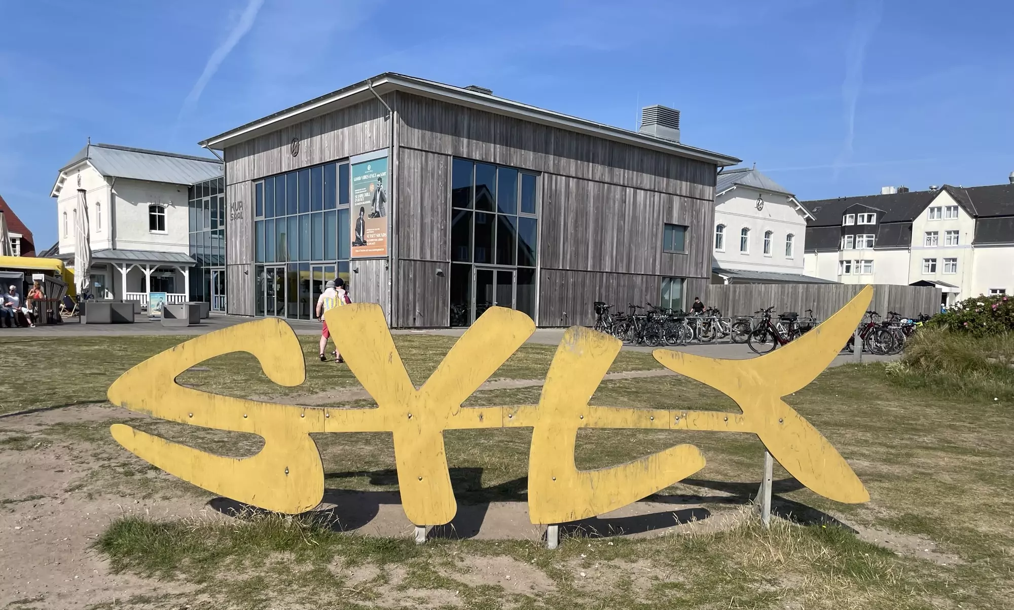 Großes Fisch-Syltzeichen aus Holz. Im Hintergrund die Kurhalle in Wenningstedt.