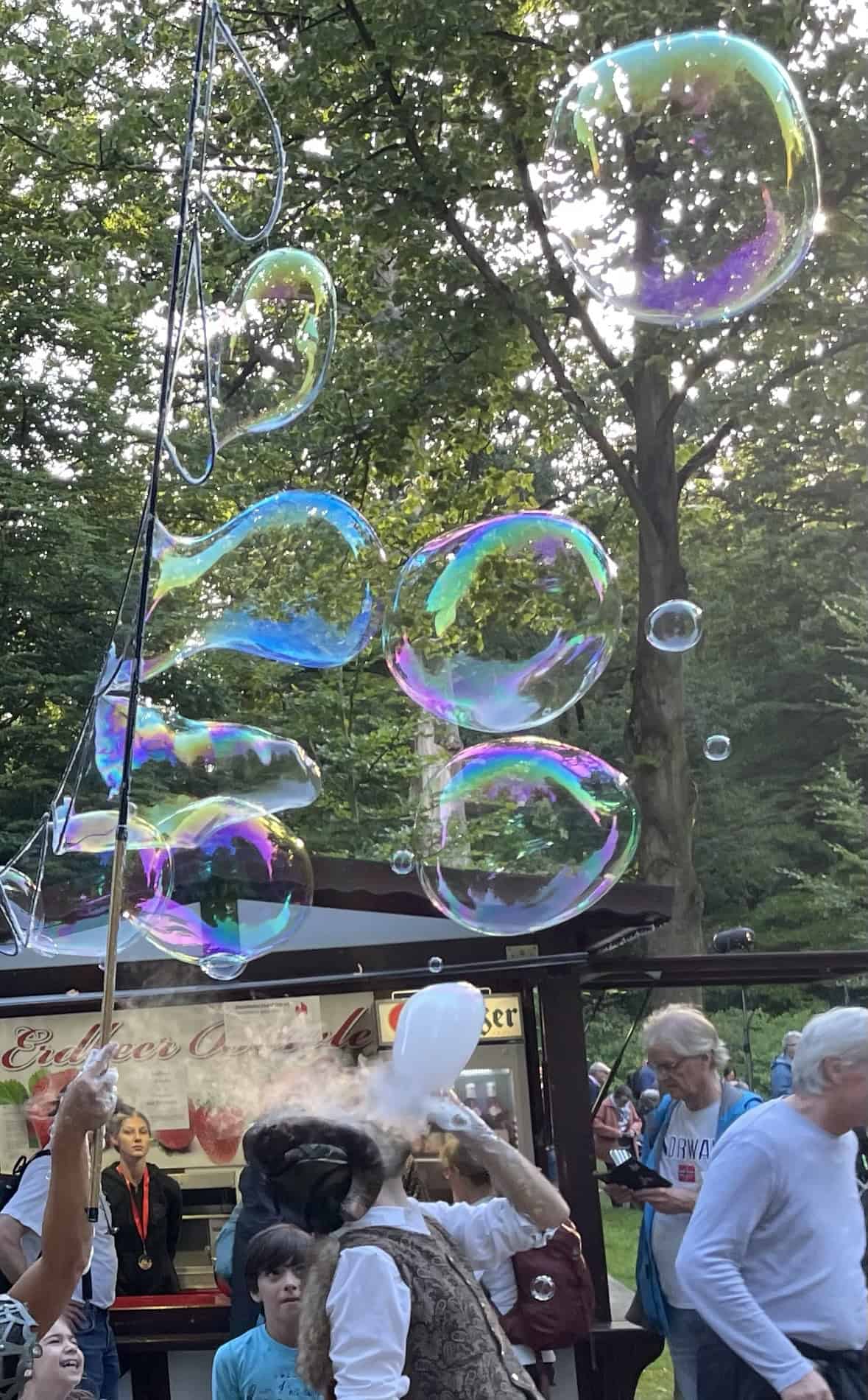 Sehr große Seifenblasen in der Luft, Zuschauer gehen den Weg entlang.