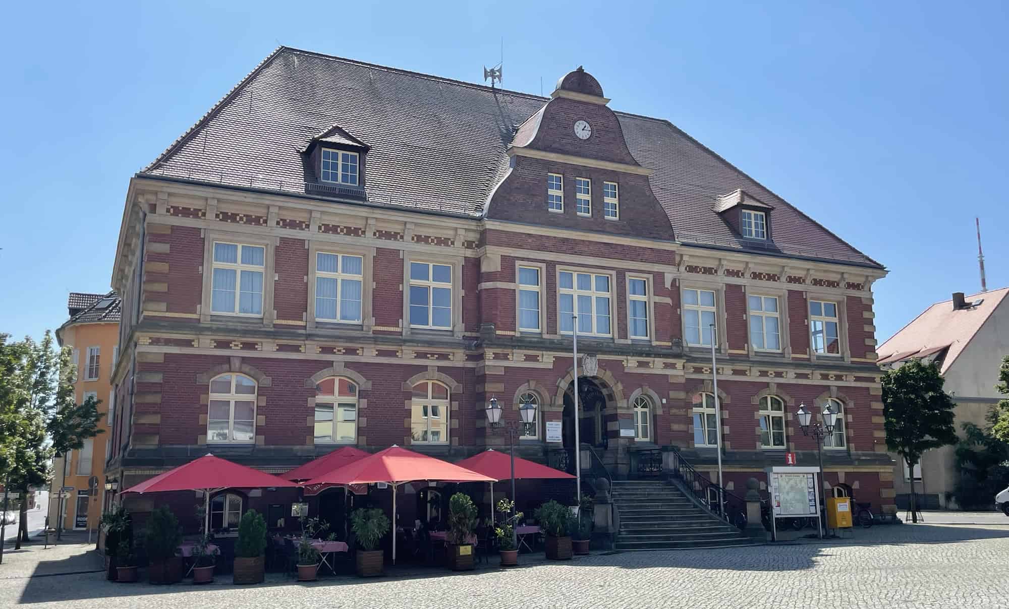 Wohl das Standesamt in Calau: Größes rotes Backsteingebäudw mit Restauration und Sonnenschirmwn davor.