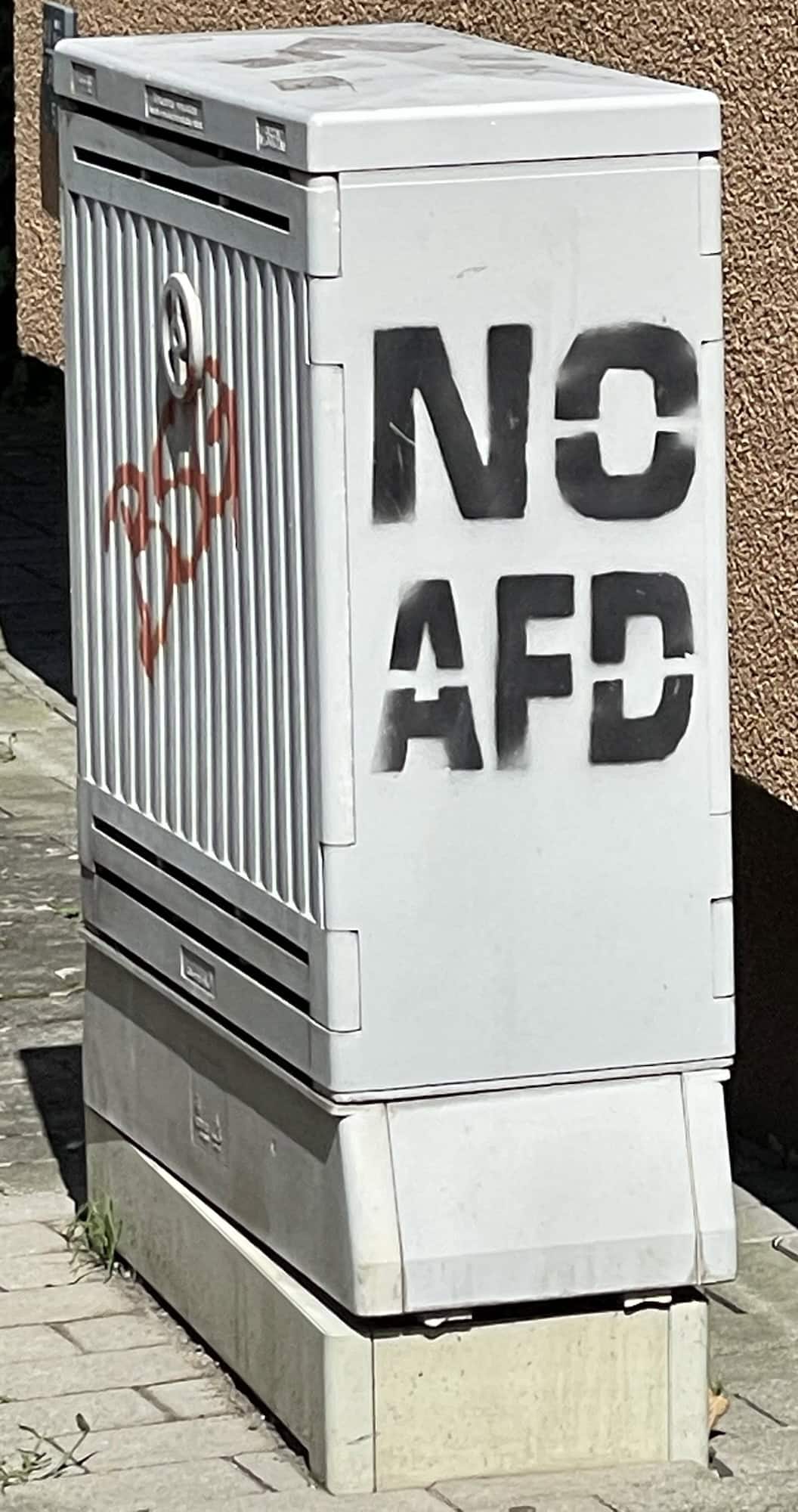 Grauer Kasten vor Häuserwand mit Aufschrift: NO AFD.