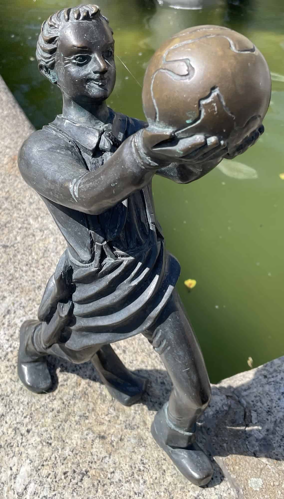 Metallfigur hält Welt in den Händen am Brunnen.