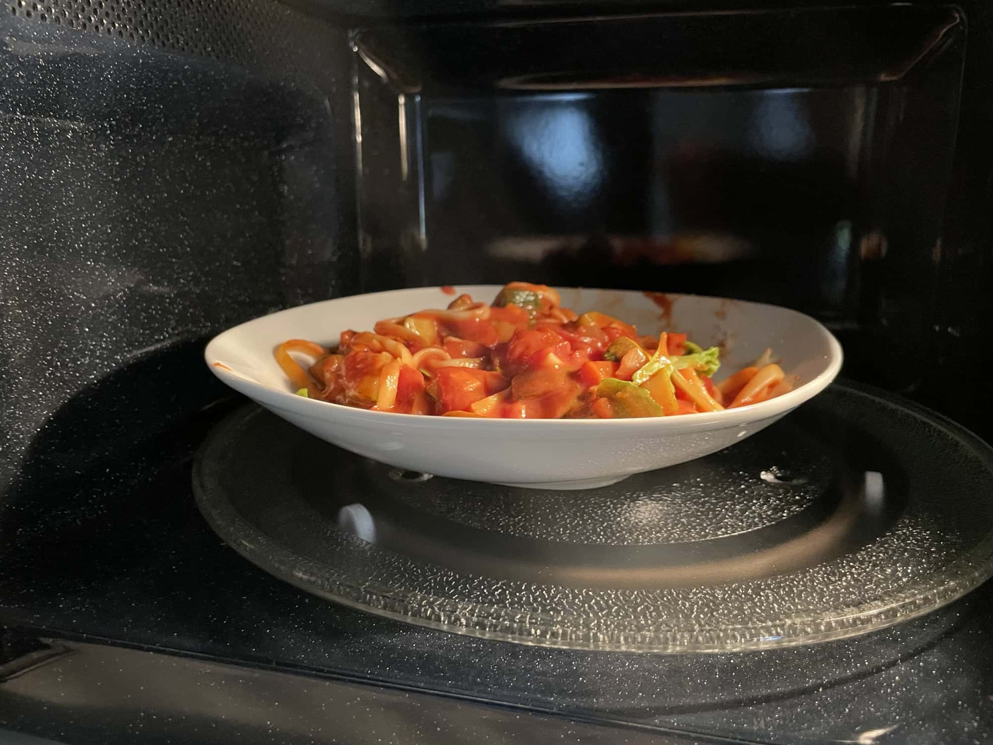 Blick in eine Drehtellermikrowelle mit weißem tiefen Teller mit Pasta ind roter Nudelsauce.