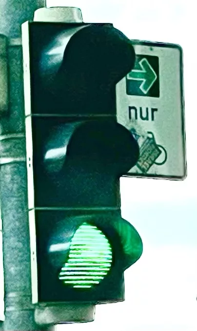 Geüne Ampel mit Schild rechts davon mit grünem Rechtsabbiegepfeil für Fahrräder, wobei das Fahhradsymbol dtark mit einem Aufkleber verdeckt ist.