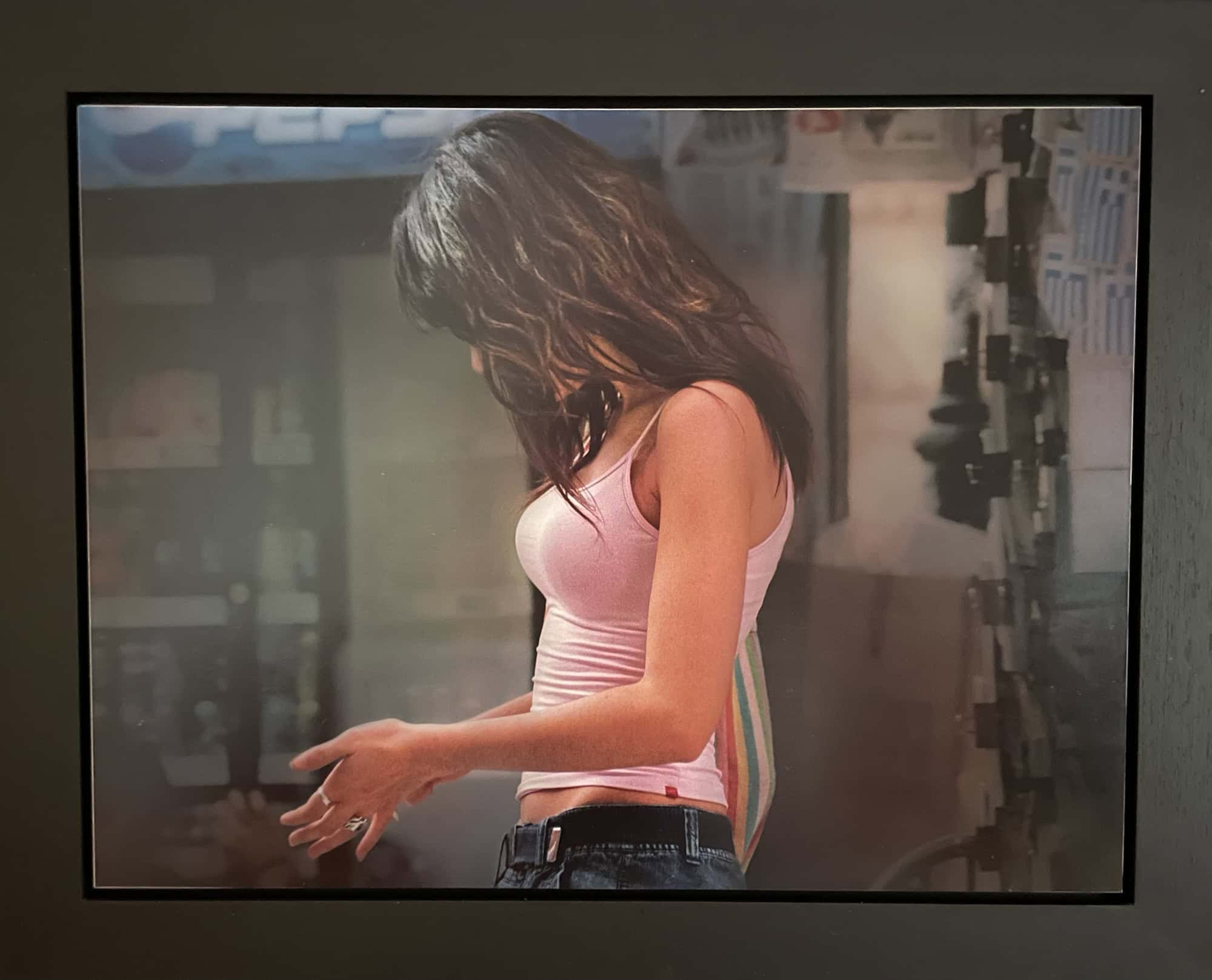 Gemälde einer fotorealistischen Feau, lange schwarze Haare, die das Gesicht verdecken (sie steht seitlich), rosa ärmelloses Top und Blue Jeans. Hintergrund ist recht dunkel, schwint auf einem Balkon zu sein.