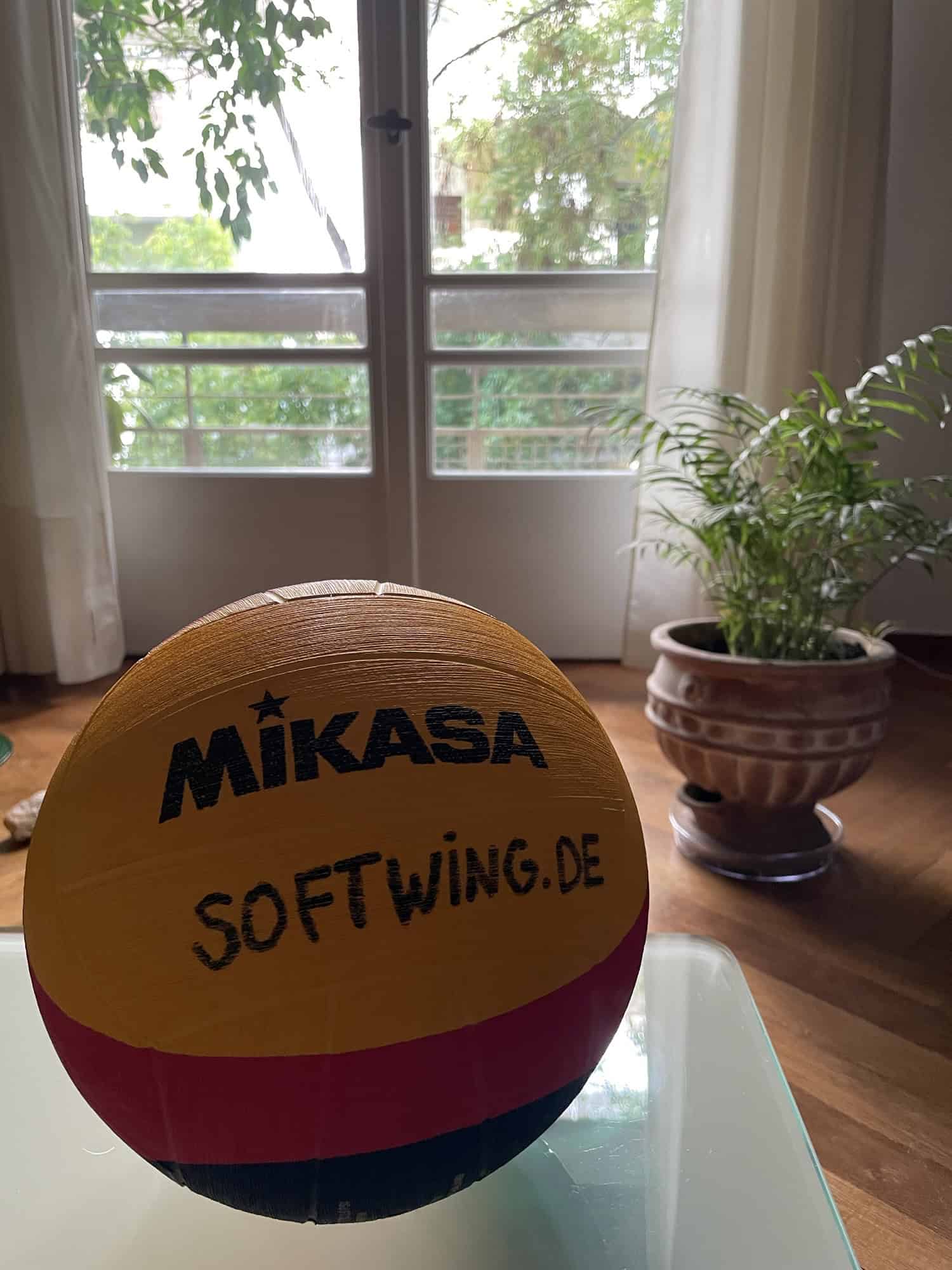 Wasserball im Raum auf Glascouchtisch, im Hintergrund rechts Topfpflanze und Fenster hinten.