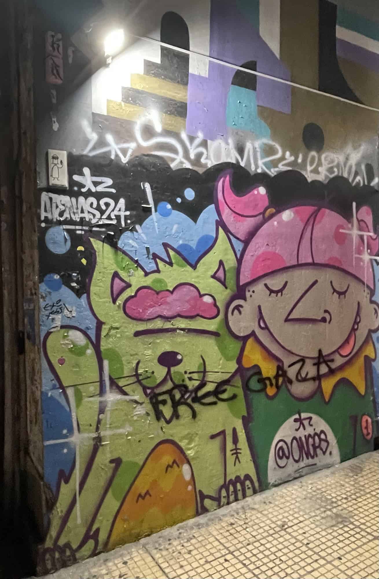 An Wand: Winkende grüne Katze und Männchen mit rosa Helm.