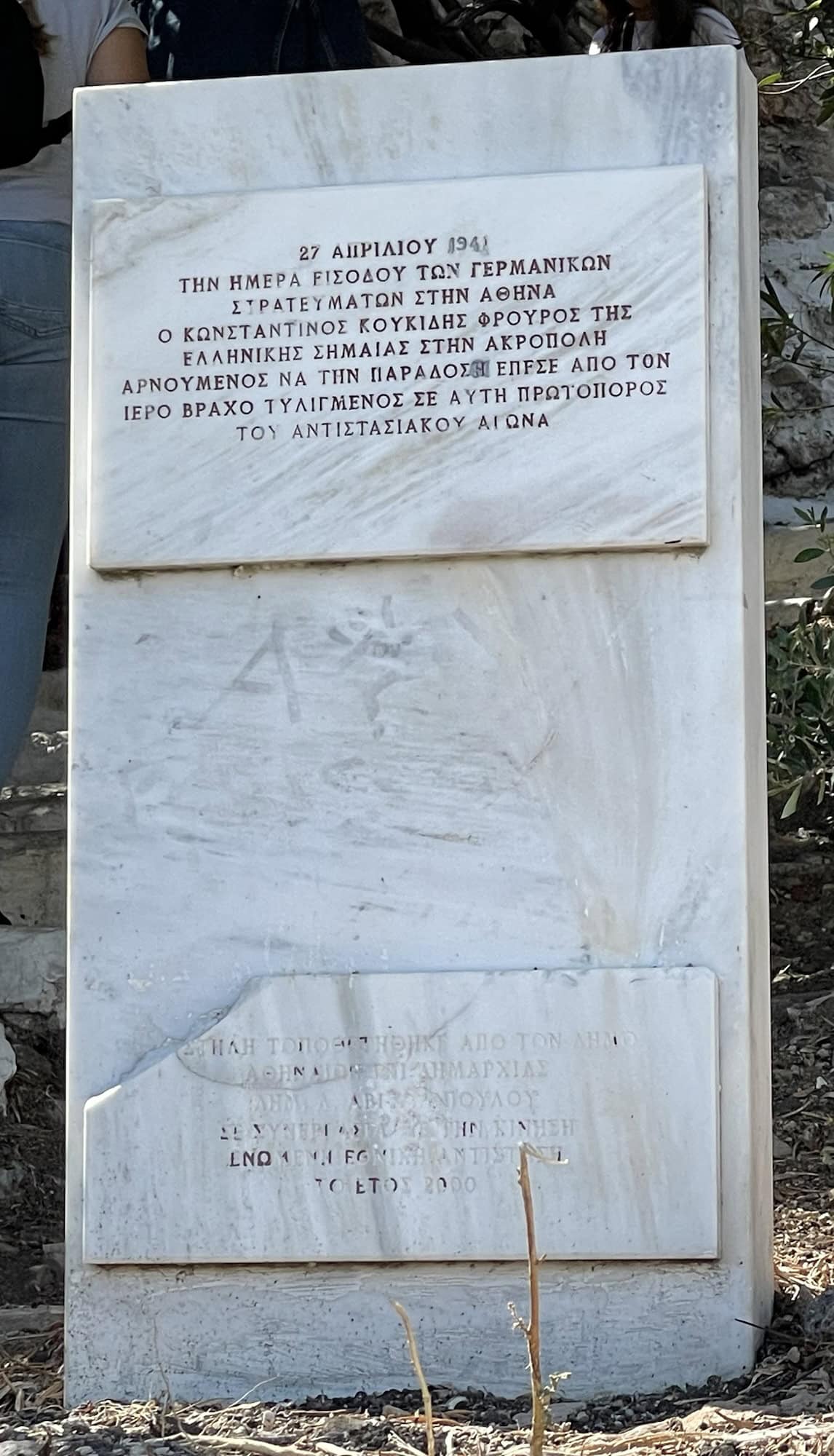 Erinnerungsstein mit Innschrift zur Erinnerung an Widerstand gegrn die Nazi-Eroberung Athens und die griechische Fahne auf der Akropolis.