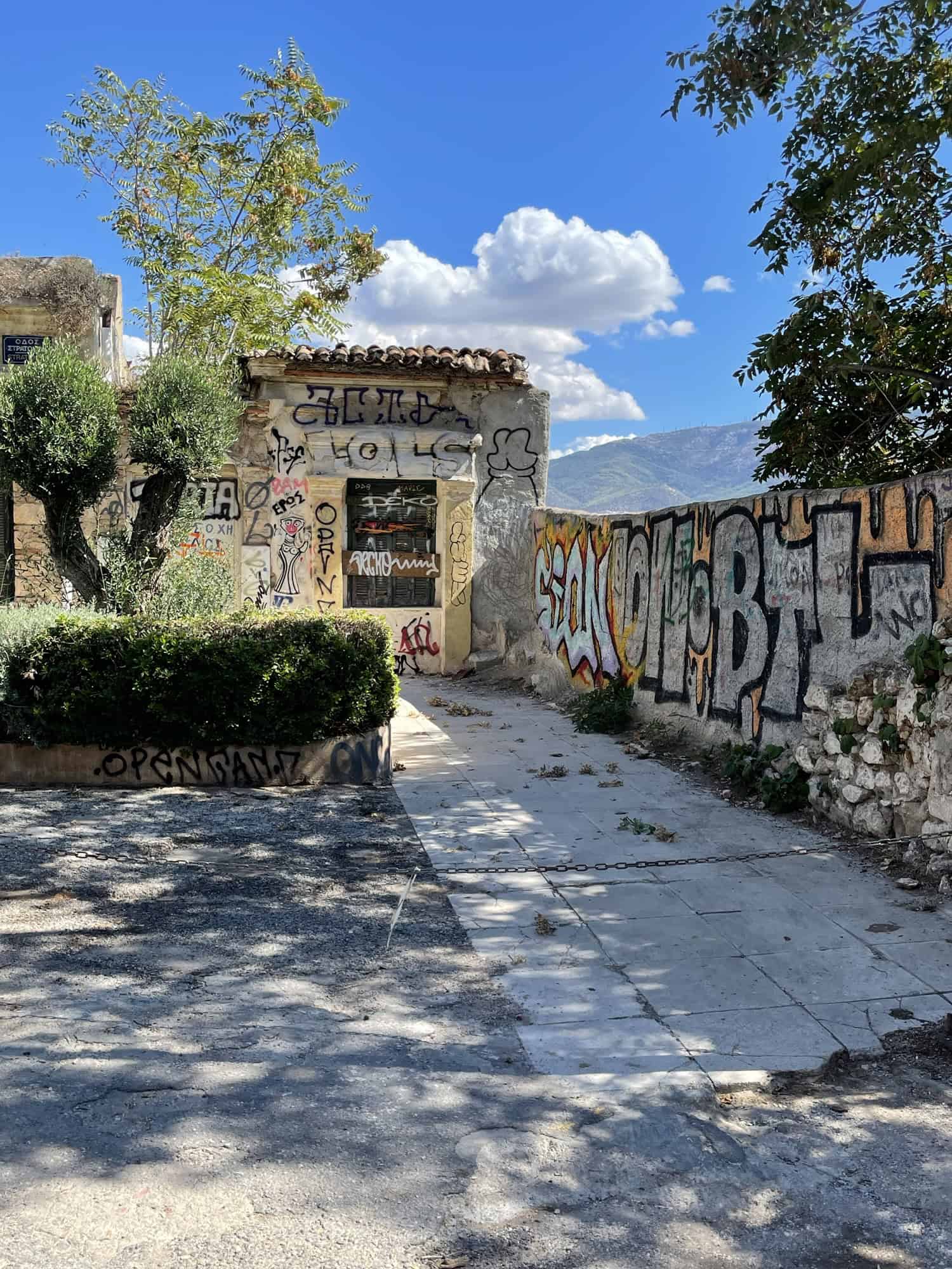 Rechts Steinwand mit Graffitis, hibten ein Steinhäuschen, im Hintergrund ein Berg/Hügel.