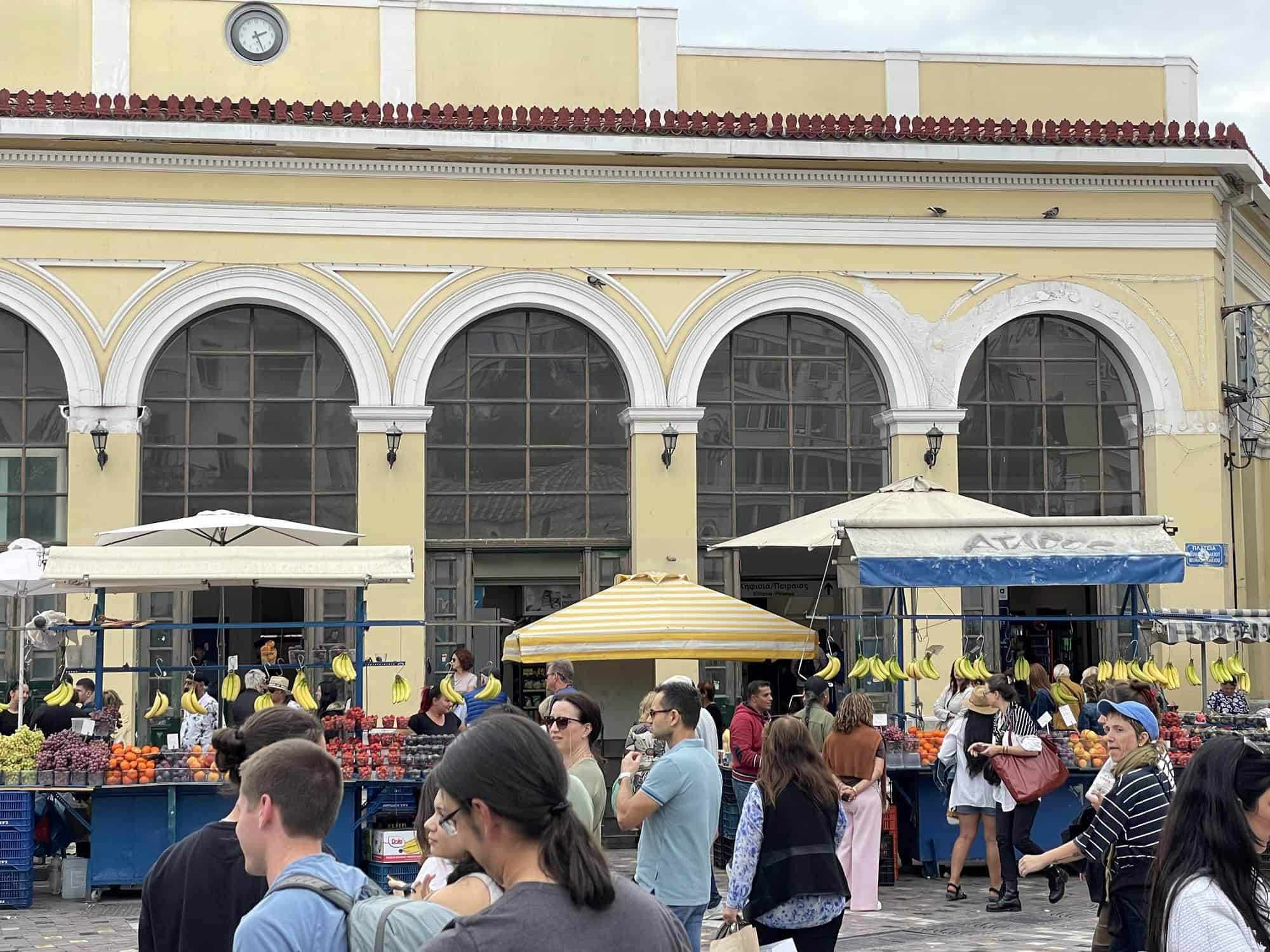 Helles Gebäude, davor Stände, die Bananen und anderes Obst verkaufen.