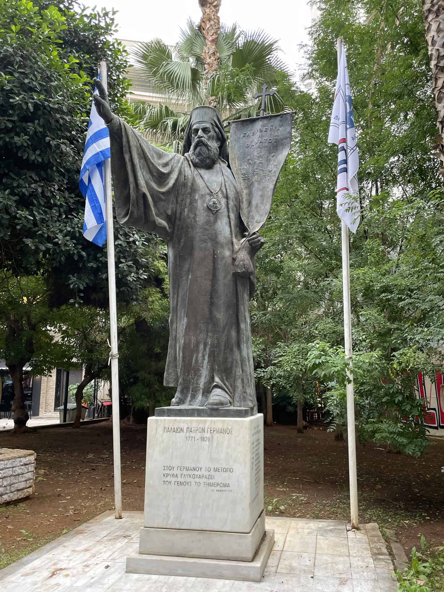 Statue eines Geistlichen mit zwei Fahnen im Hintergrund.