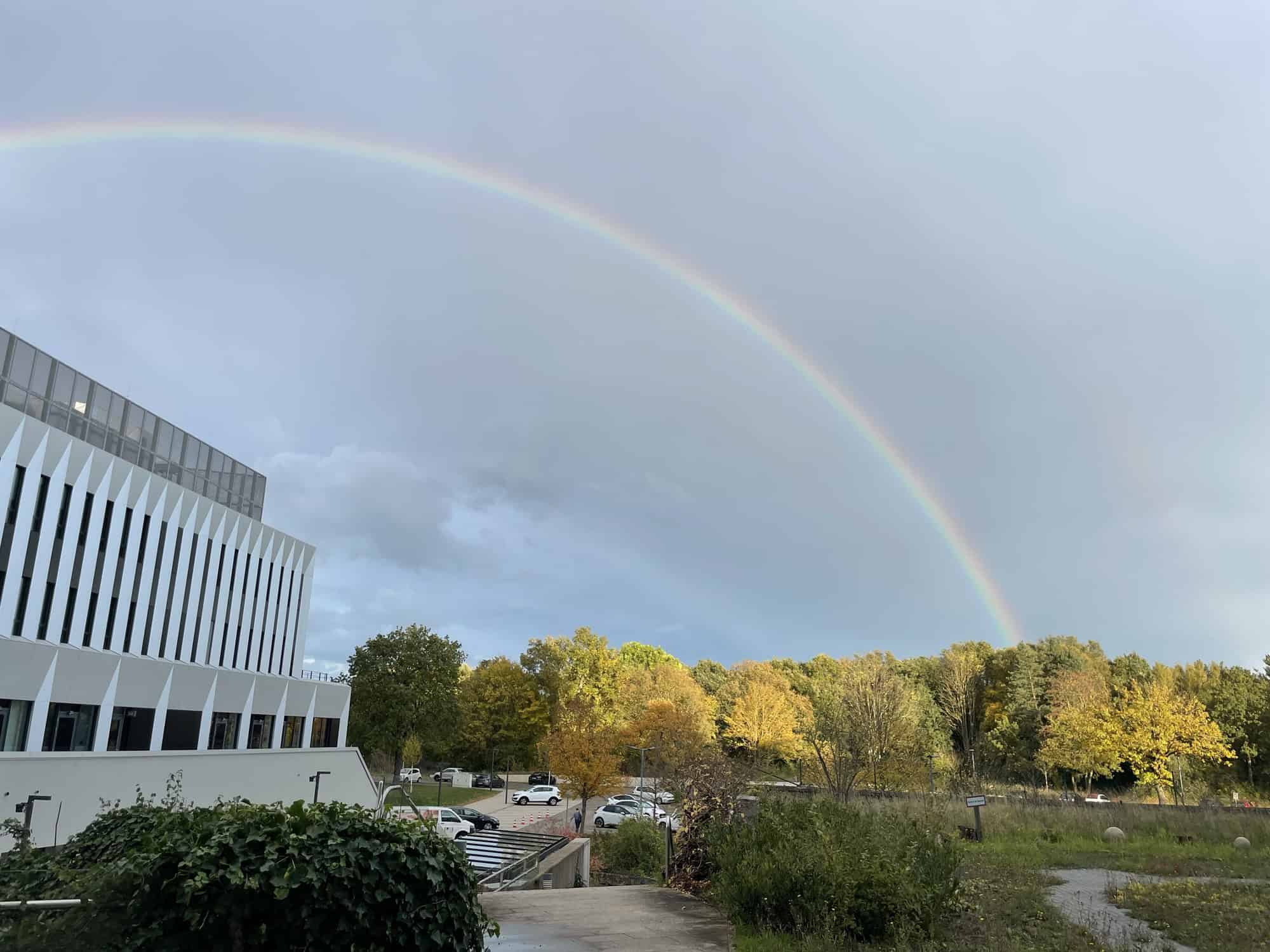 Regenbogen von rechts unten nach links oben, links im Vordergrund der Karrierecampus Hannover, rechts Böume im Hintergrund.