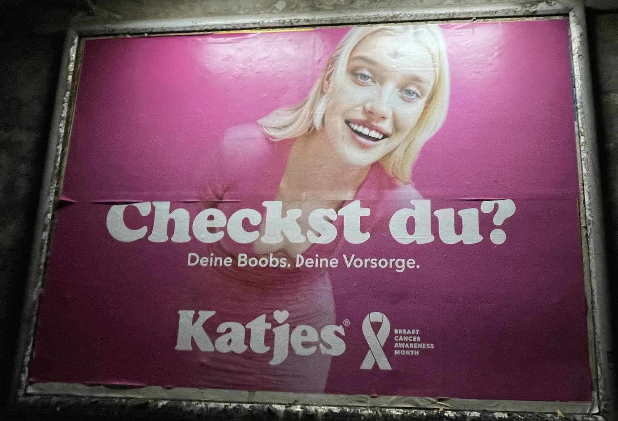 Außenwerbeplakat 'Checkst du!' rosa von Kajes mit abgebildetet Frau zum Brustkrebsmonat Oktober, hellhäutige blonde Frau in rosa Kleid.