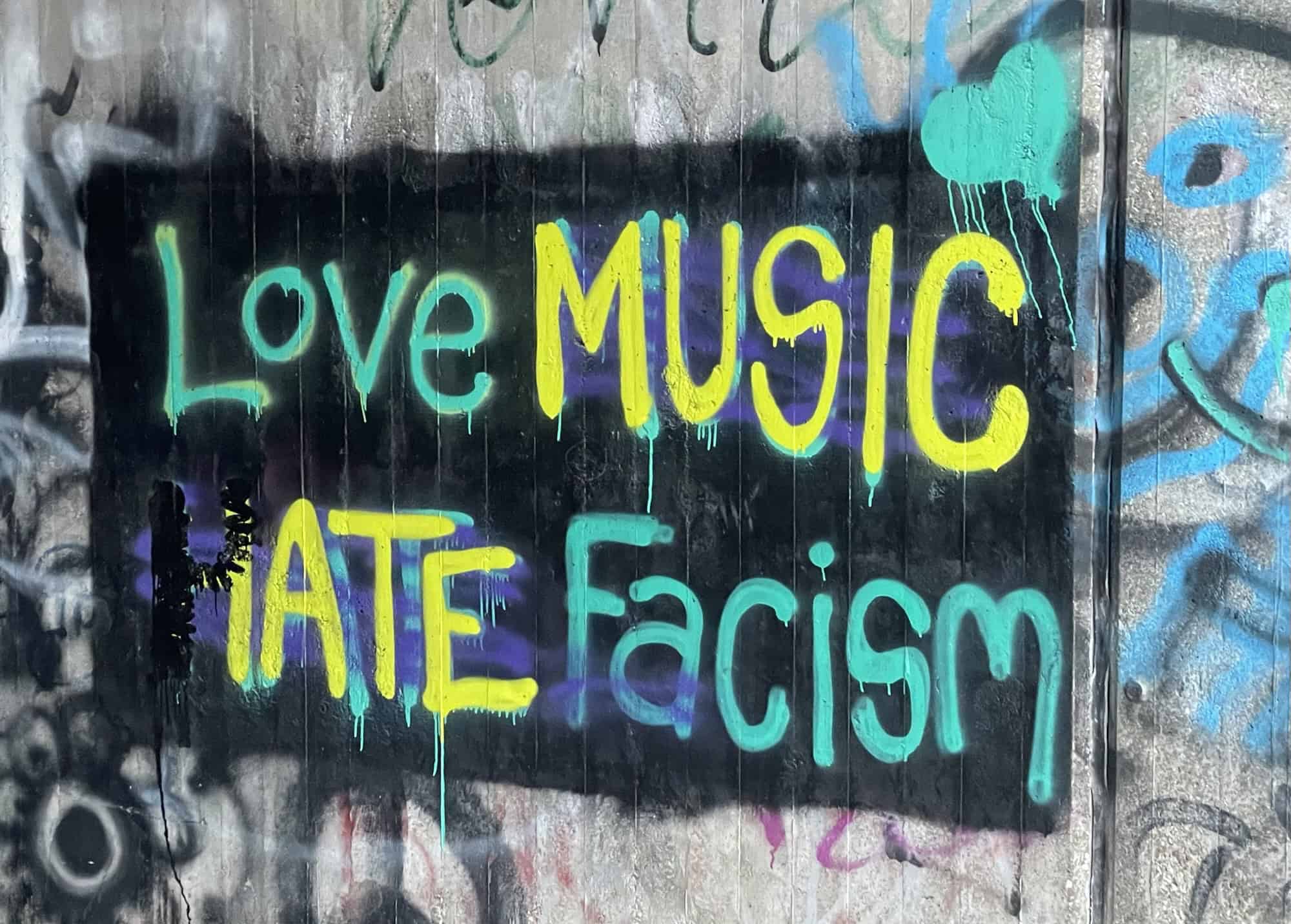 Graffiti 'Love music hate facism' in grün-gelber Schrift mit schwarzem Hintergeund auf Betonwand.