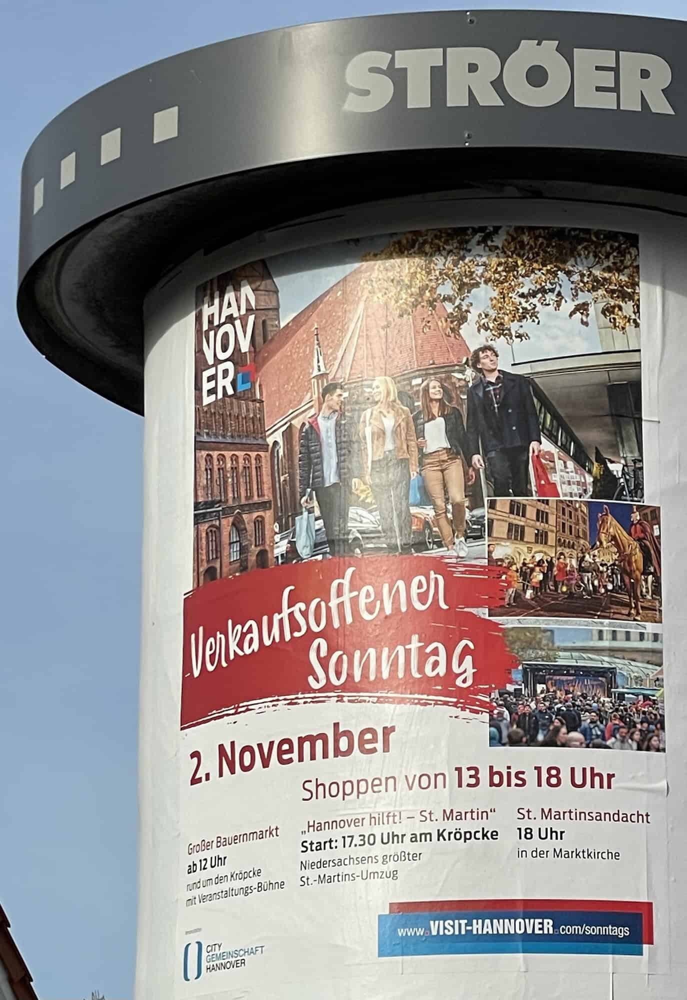 Litfaßsäule mit Metallkranz oben und Werbung für einen Verkaufsoffenen Sonntag.