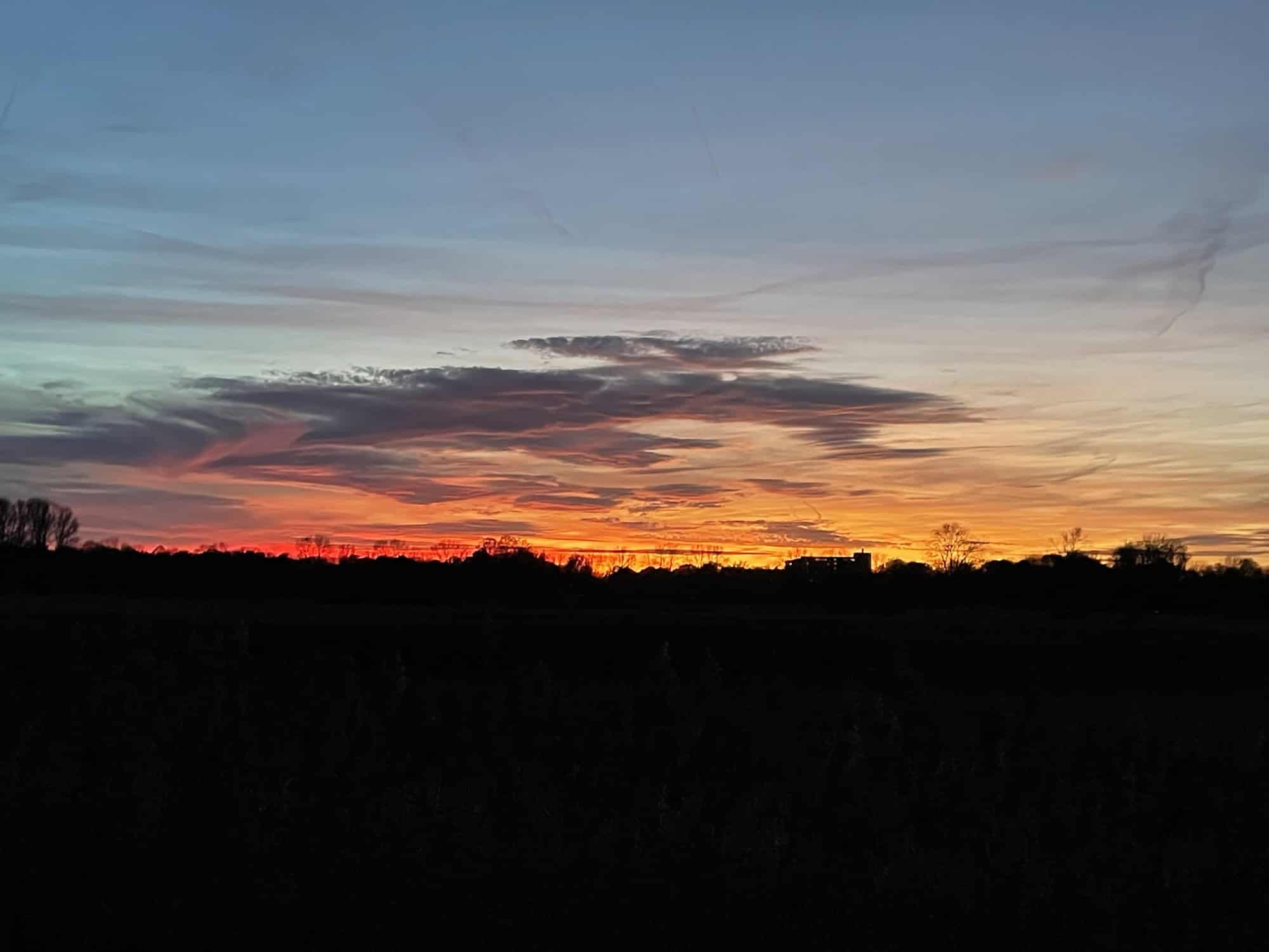 Schwarzer Streifen unten, darüber orange-roter Himmelsstreifen , Wolke und hellblauer Himmel.