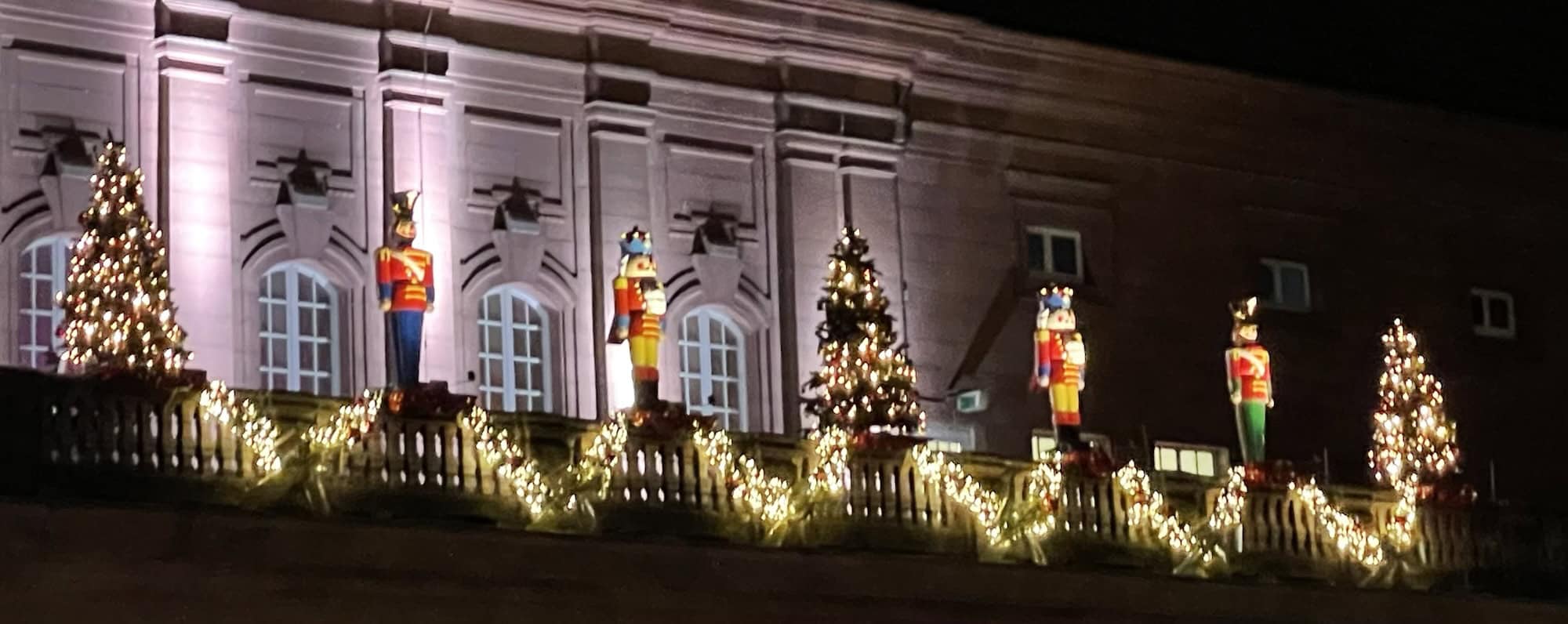 Auf der rechten Seite angeleuchtete Großnußknackerfigufren auf dem Balkon des Bahnhofsgebäudes.