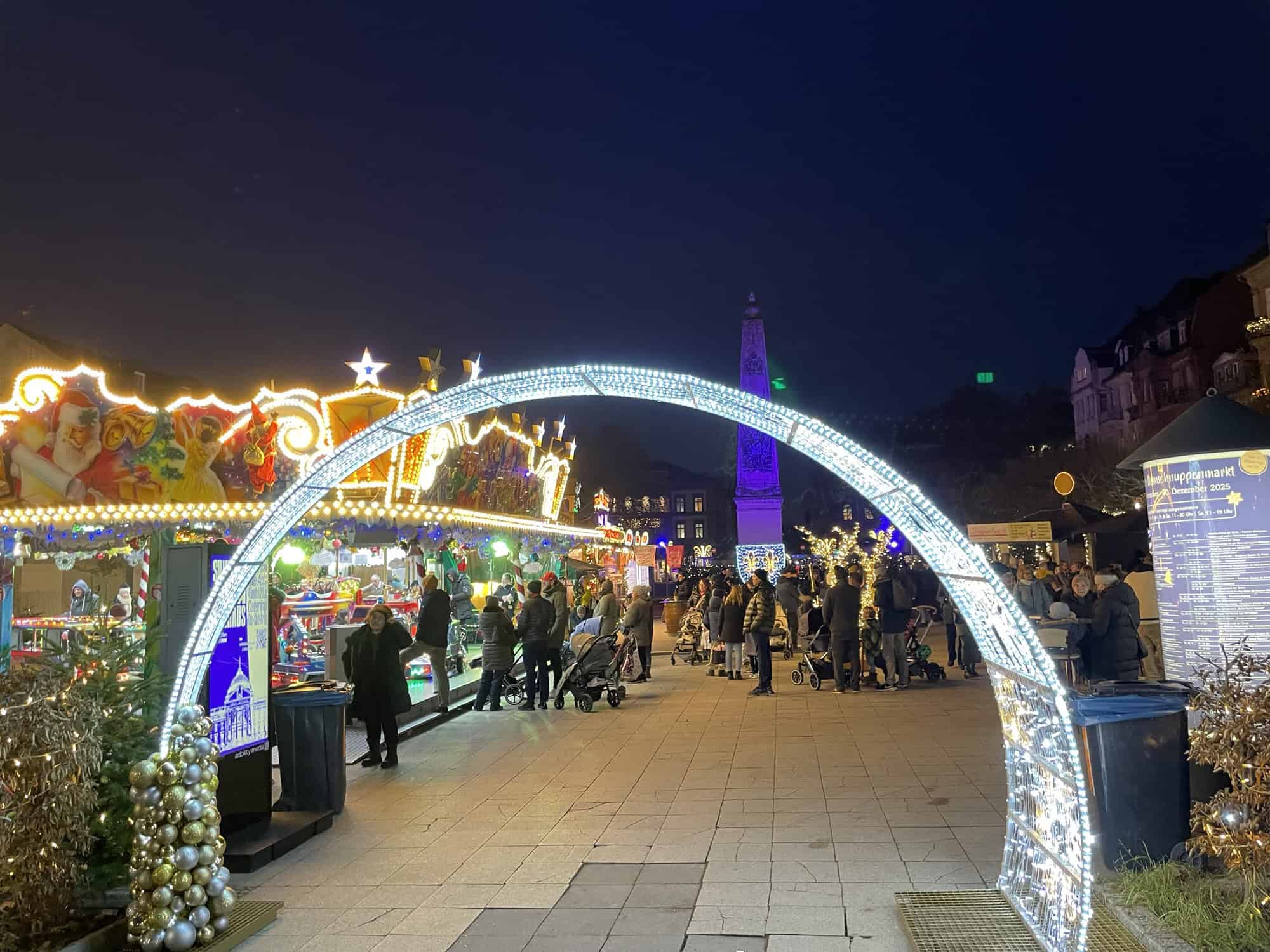 Eingang des Weihnachtsmarktes mit leuchtendem Torbogen und Weihnachtsmarktbuden dahinter.