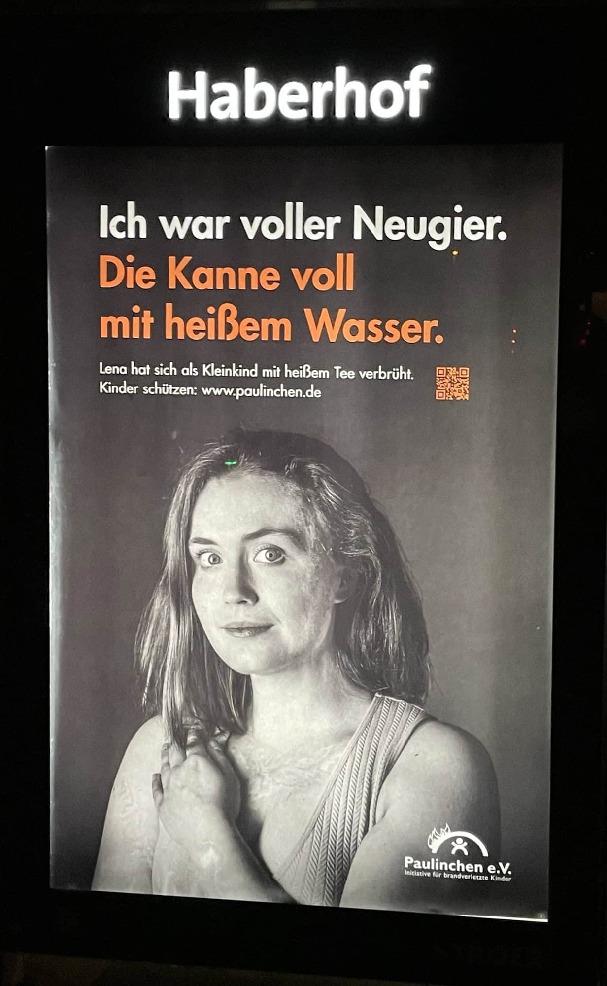Außenreklame: Schwarweißportrait einer Frau (Oberkörper) mit Vernarbungen auf dem Dekoltet: Ich war voller Neugier. Die Kanne voll mit heißem Wasser. Paulinchen e.V. - Initiative für brandverletzte Kinder