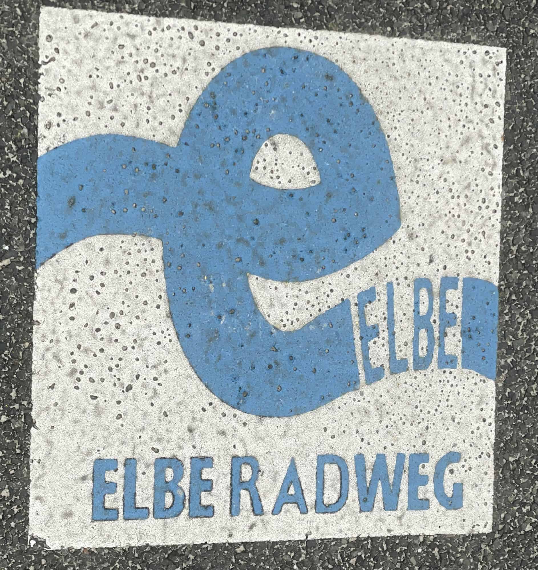 Blau-grün-gelbes Weser-Radweg-Zeichen auf dem Asphalt.
