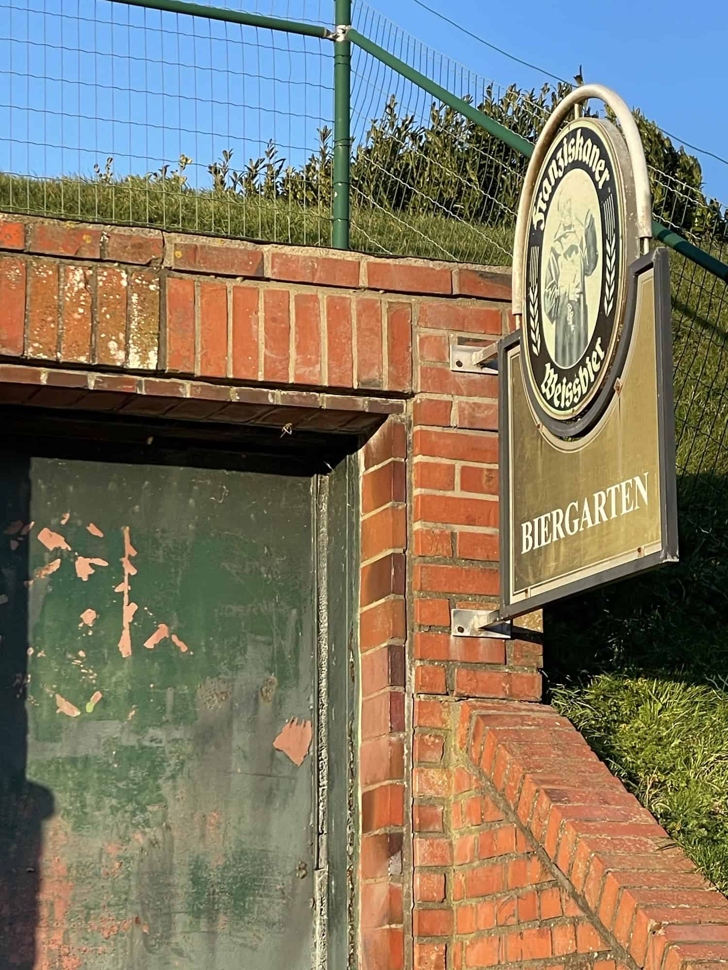 Biergartenschild mit Franziskanerreklame an Eingangstür in den Deich.