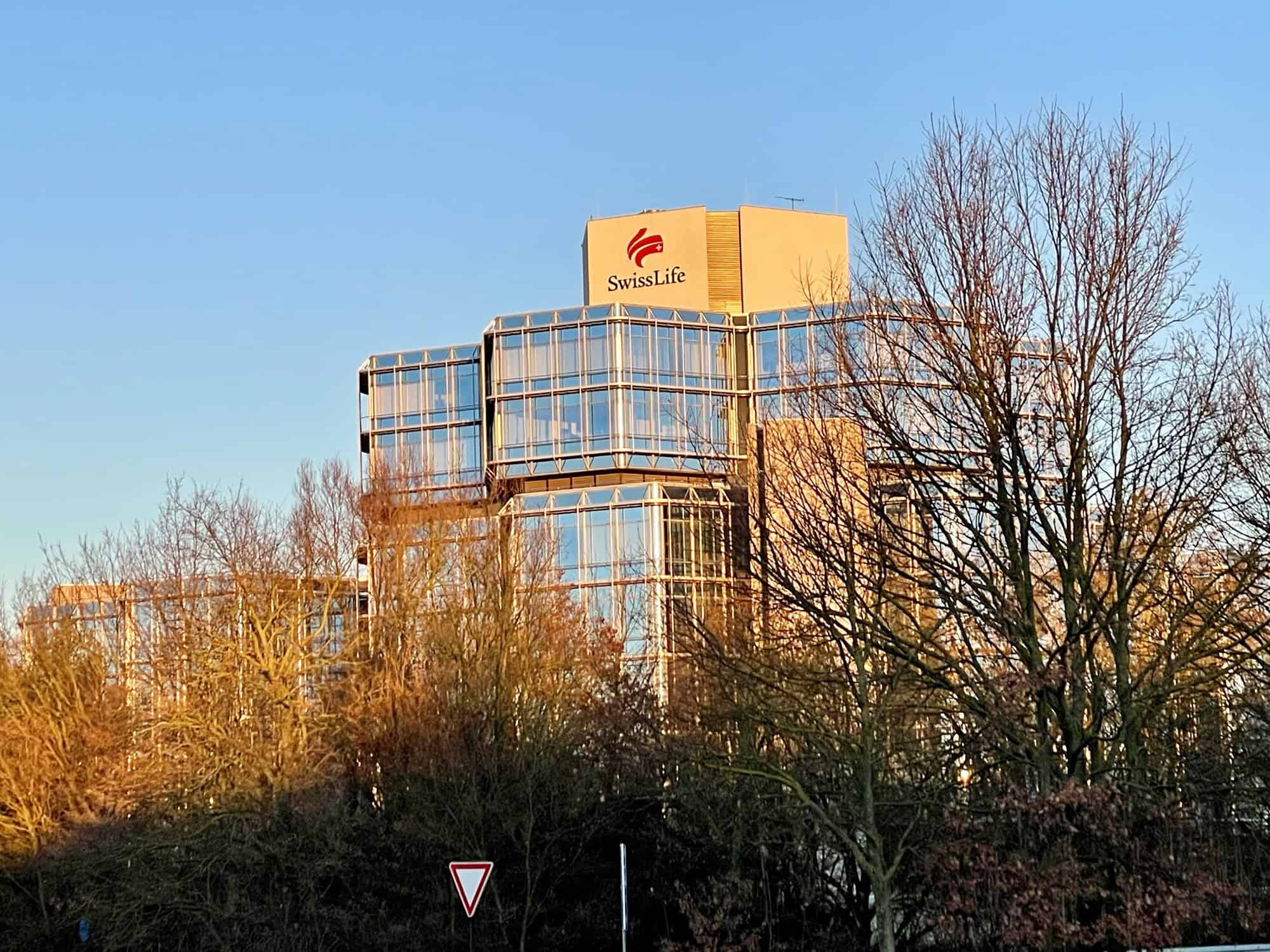 Swiss Life Gebäude in Lahe in der Sonne und von Bäumen umgeben.