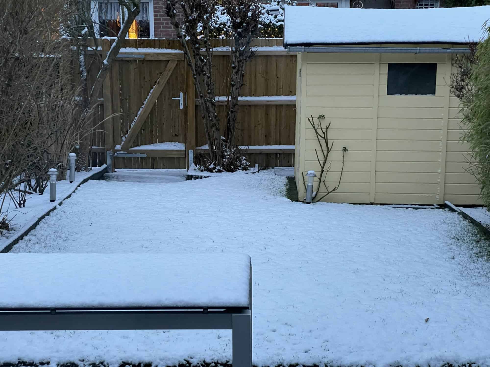 Schneebild des Gartens mit verschneitem Tisch, Rasen und Gartenschuppen.