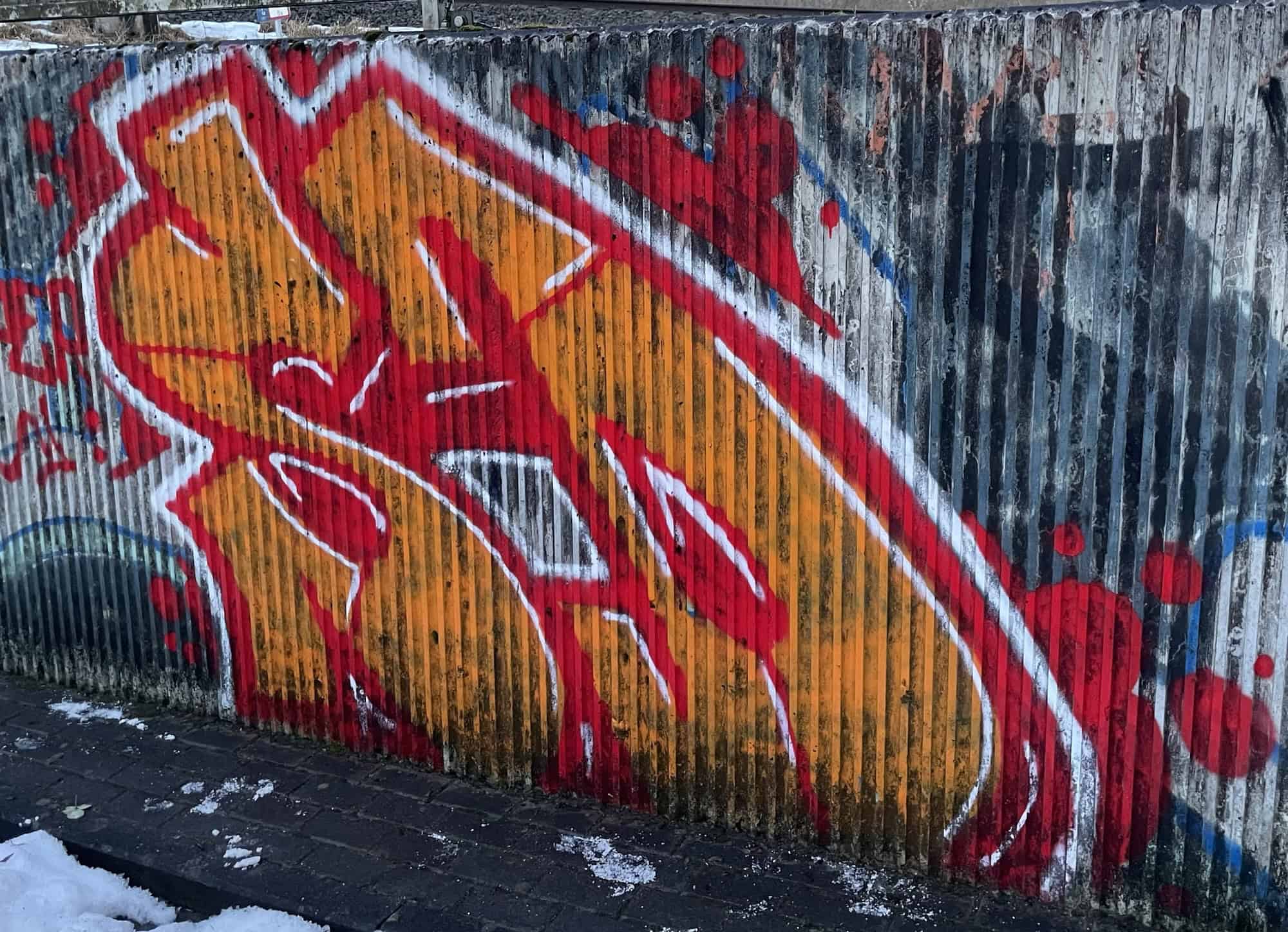Buntes Graffiti mit gelb-rotem Tagging an Betonunterführung.