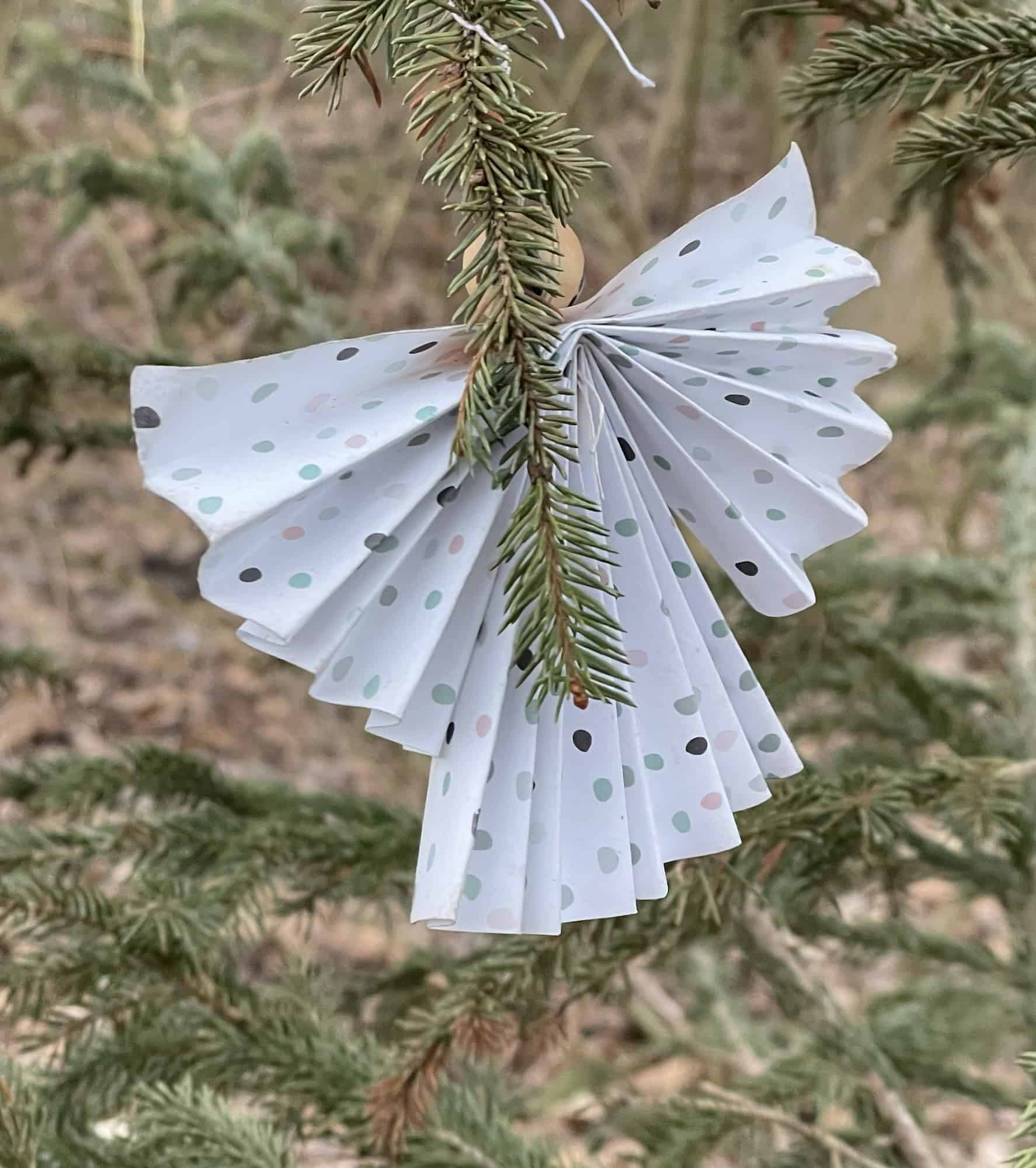 Papierengel hängt im Tannenbaum draußen im Grünen.