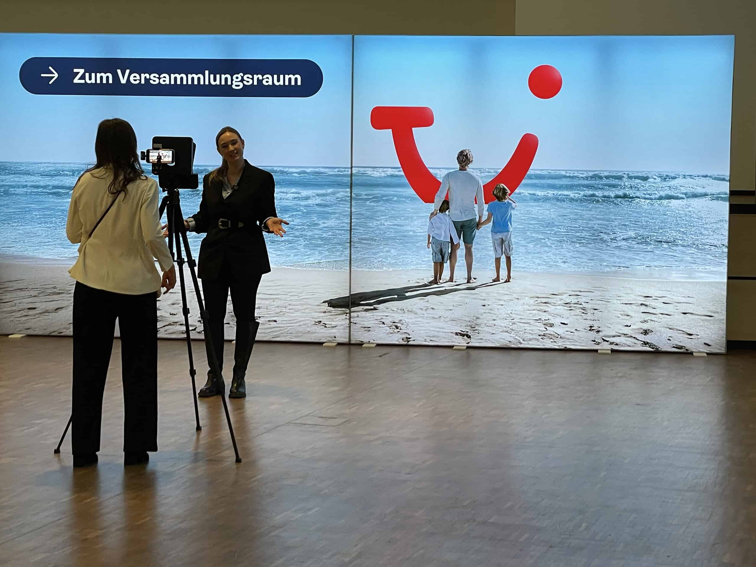 Fotografin mit Aktionärin vor TUI-Wand.