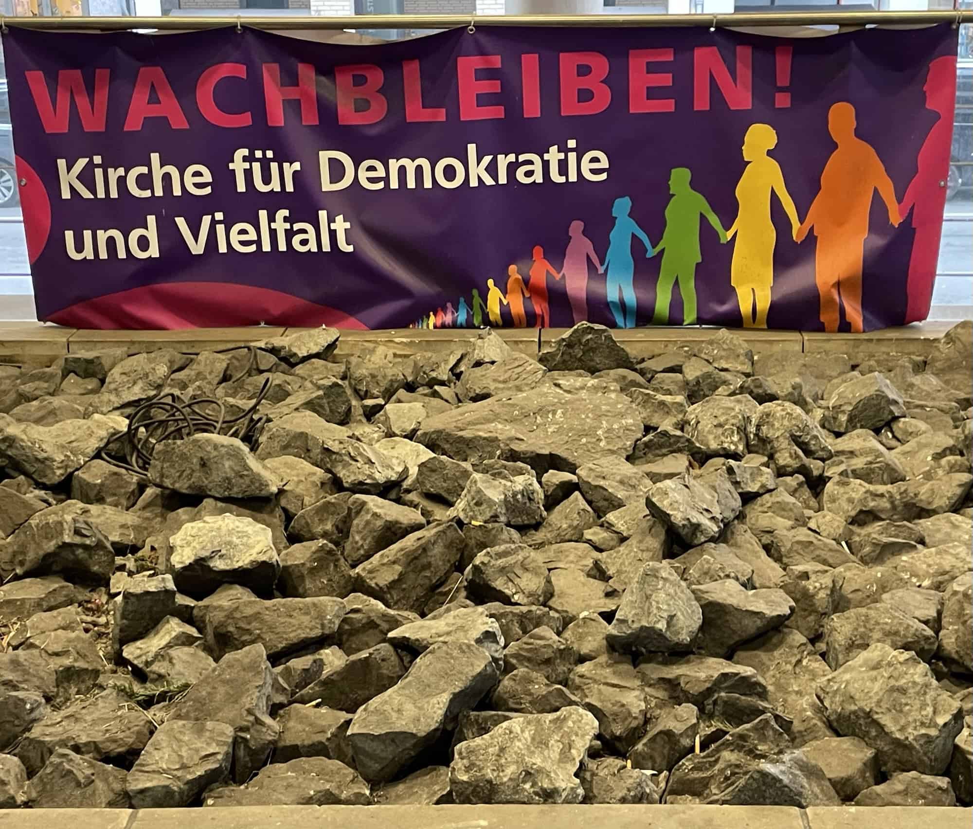 Plakat 'Wachbleiben Kirche für Demokratie und Vielfalt' vor Steinfeld.