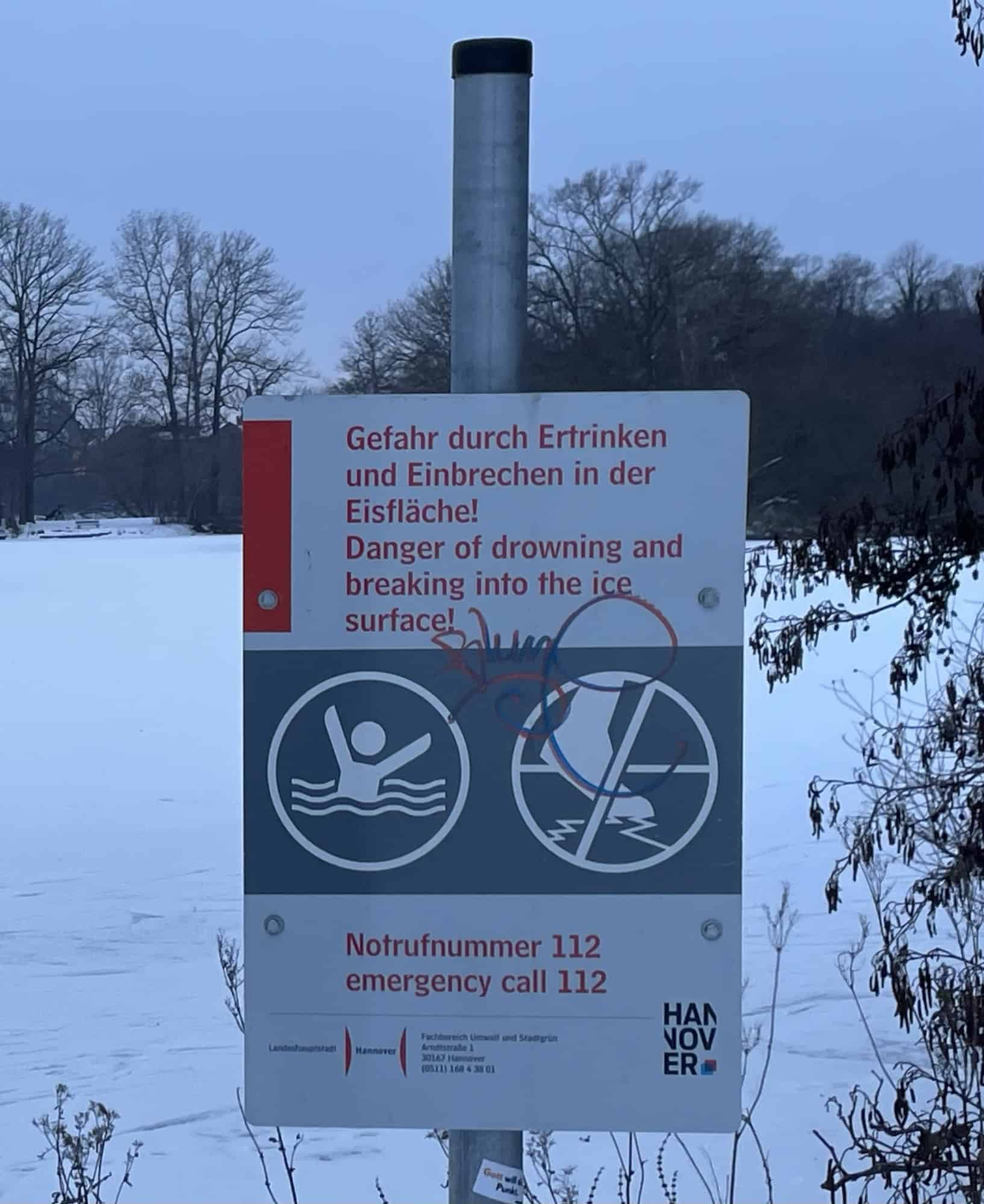 Winterbild mit Teich und Gefahrenschild vor Einbrechrn ins Eis und Ertrinkken.