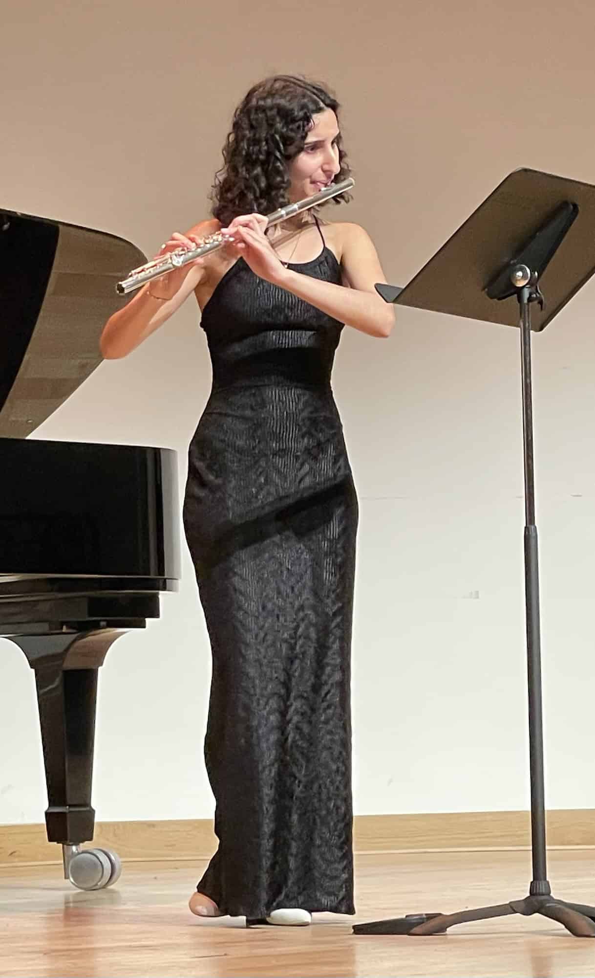Die Flötenspielerin beim Spiel auf der Bühne im langen schwarzen Kleid vor Flügel und Notenständer.