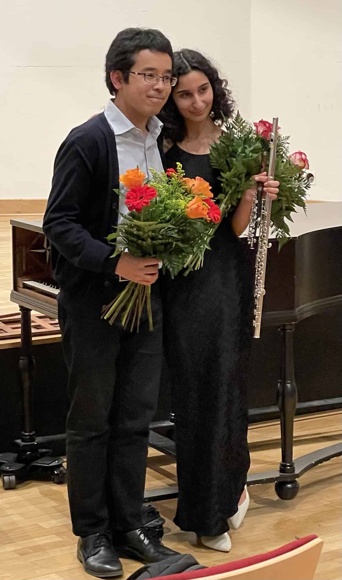 Pianist und Flötenspielerin stehen zusammen mit Blumen in een Händen.