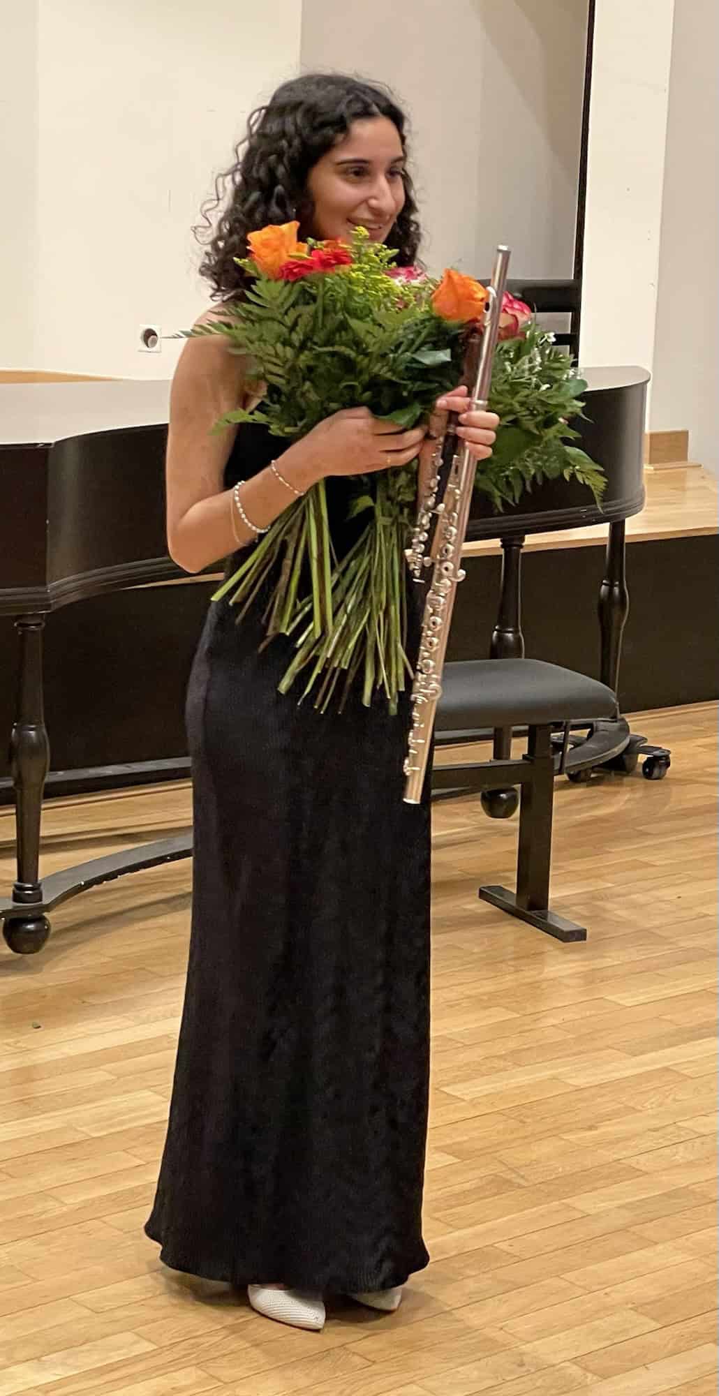 Die Flötensolistin steht mit einem riesigen Blumendtrauß und Flöte.