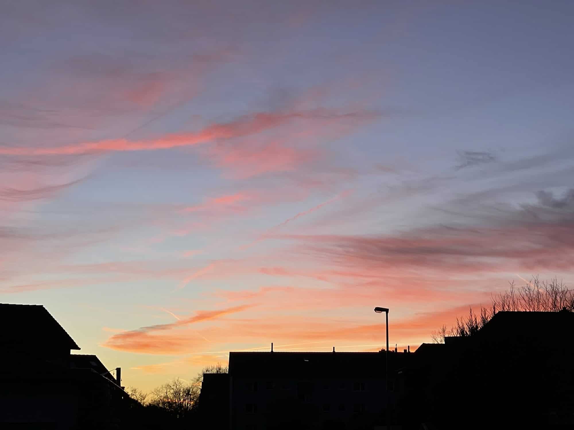 Schwarze Häusersilhouette mit blau, orange, rotem Himmel.